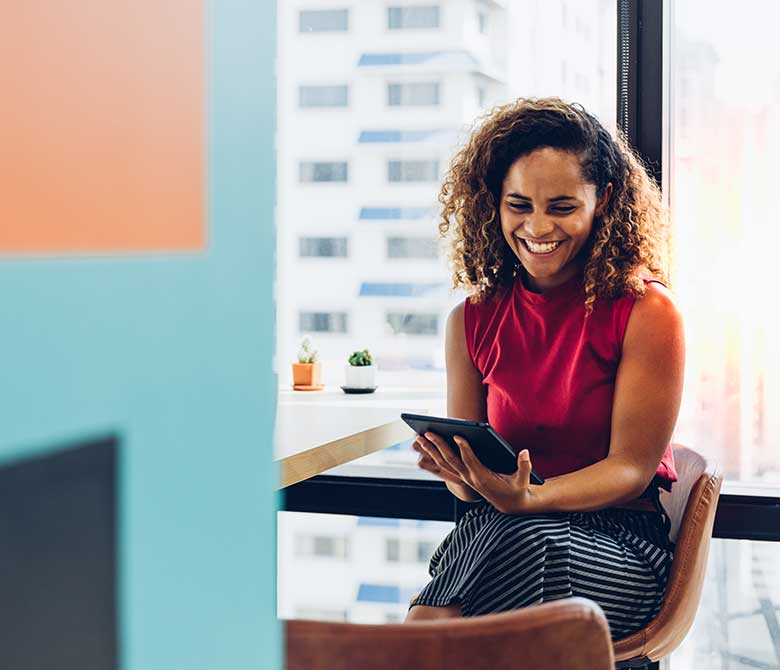 Young black woman sitting in office smiling on her tablet device.