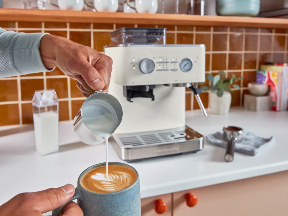 Semi-automatic-espresso-machine-with-burr-grinder-5KES6551-person-making-latte-art-in-front-of-coffee-machine-in-almond-cream