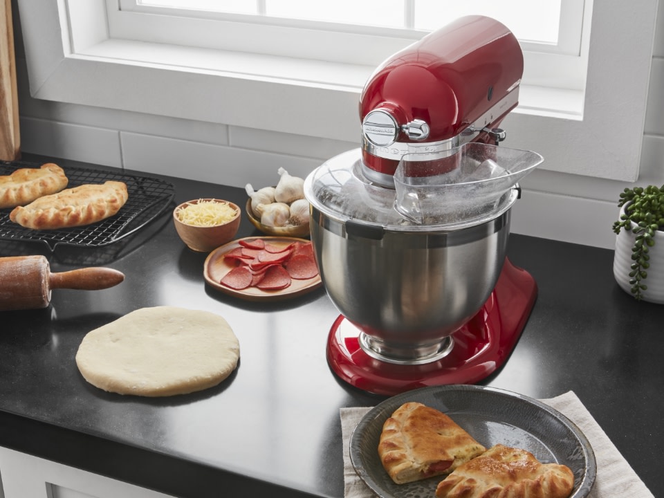 Stand-mixer-and-pourig-shield-with-pie-and-raw-dough-on-kitchen-counter-at-window