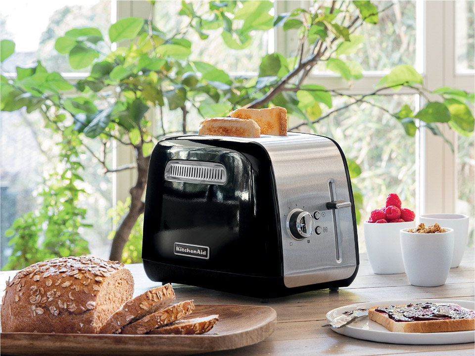 Breakfast-toaster-2-slice-classic-onyx-black-two-slices-of-toast-in-toaster-next-to-sliced-bread-and-jam-spread-on-table