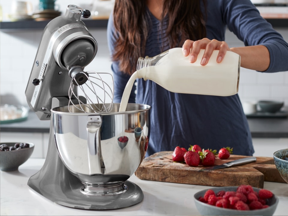 Lady-pouring-milk-into-stainless-steel-bowl-on-table-with-chopping-board-and-strawberries