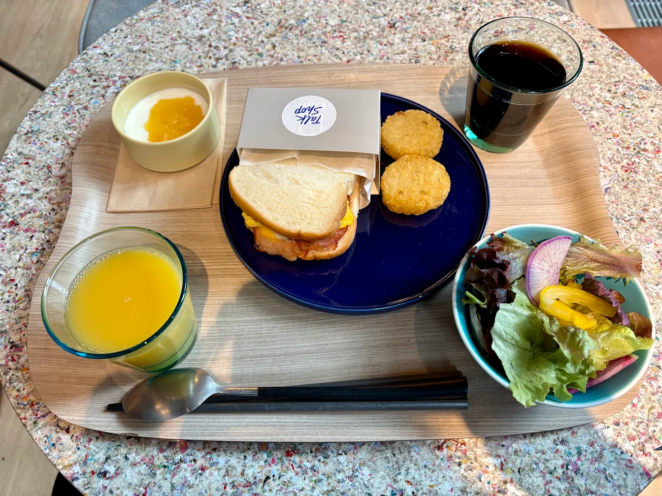 Khay breakfast với sandwich, hash brown, salad, sữa chua và nước cam