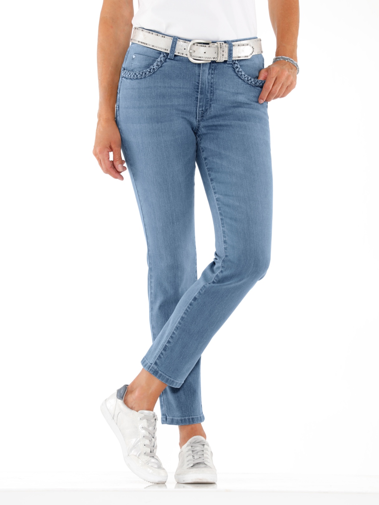 Damenjeans in Hellblau mit geflochtenen Taschen und weißem Gürtel, kombiniert mit weißen Sneakern und weißem Oberteil.