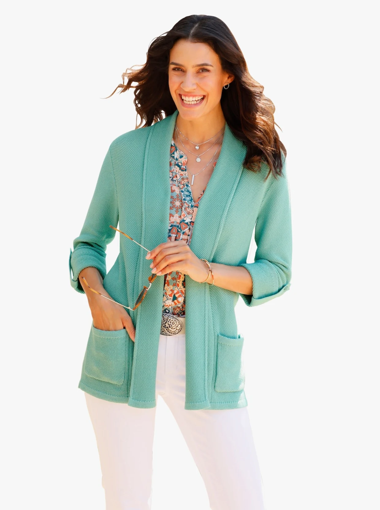 Frau mit Strickjacke mit Schalkragen in der Farbe türkis und Shirt in den Farben braun, türkis, weiß sowie weißer Hose. Frau mit Strickjacke mit Schalkragen in der Farbe türkis und Shirt in den Farben braun, türkis, weiß sowie weißer Hose.