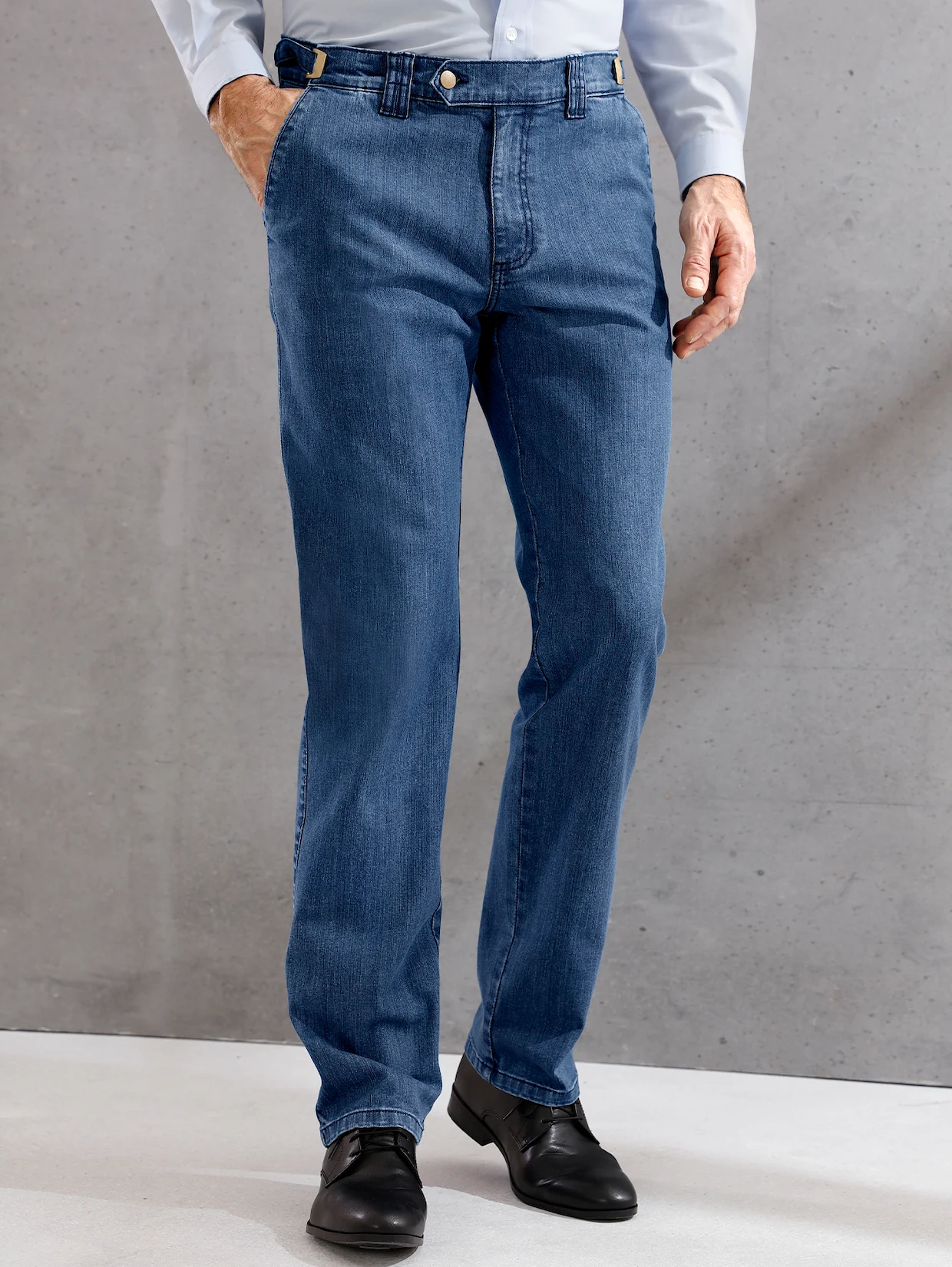 Herrenjeans in blauem Denim mit geradem Schnitt, getragen mit schwarzem Schuh und weißem Hemd vor grauem Hintergrund. Herrenjeans in blauem Denim mit geradem Schnitt, getragen mit schwarzem Schuh und weißem Hemd vor grauem Hintergrund.