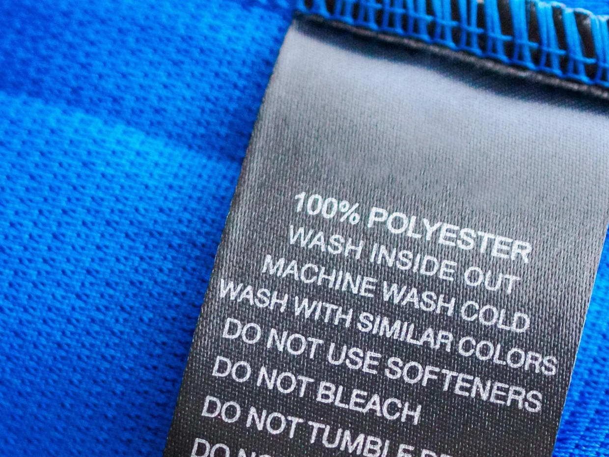 Pflegeetikett aus schwarzem Stoff mit weißer Schrift auf blauem Polyestergewebe, zeigt Wasch- und Pflegehinweise für das Material. Pflegeetikett aus schwarzem Stoff mit weißer Schrift auf blauem Polyestergewebe, zeigt Wasch- und Pflegehinweise für das Material.