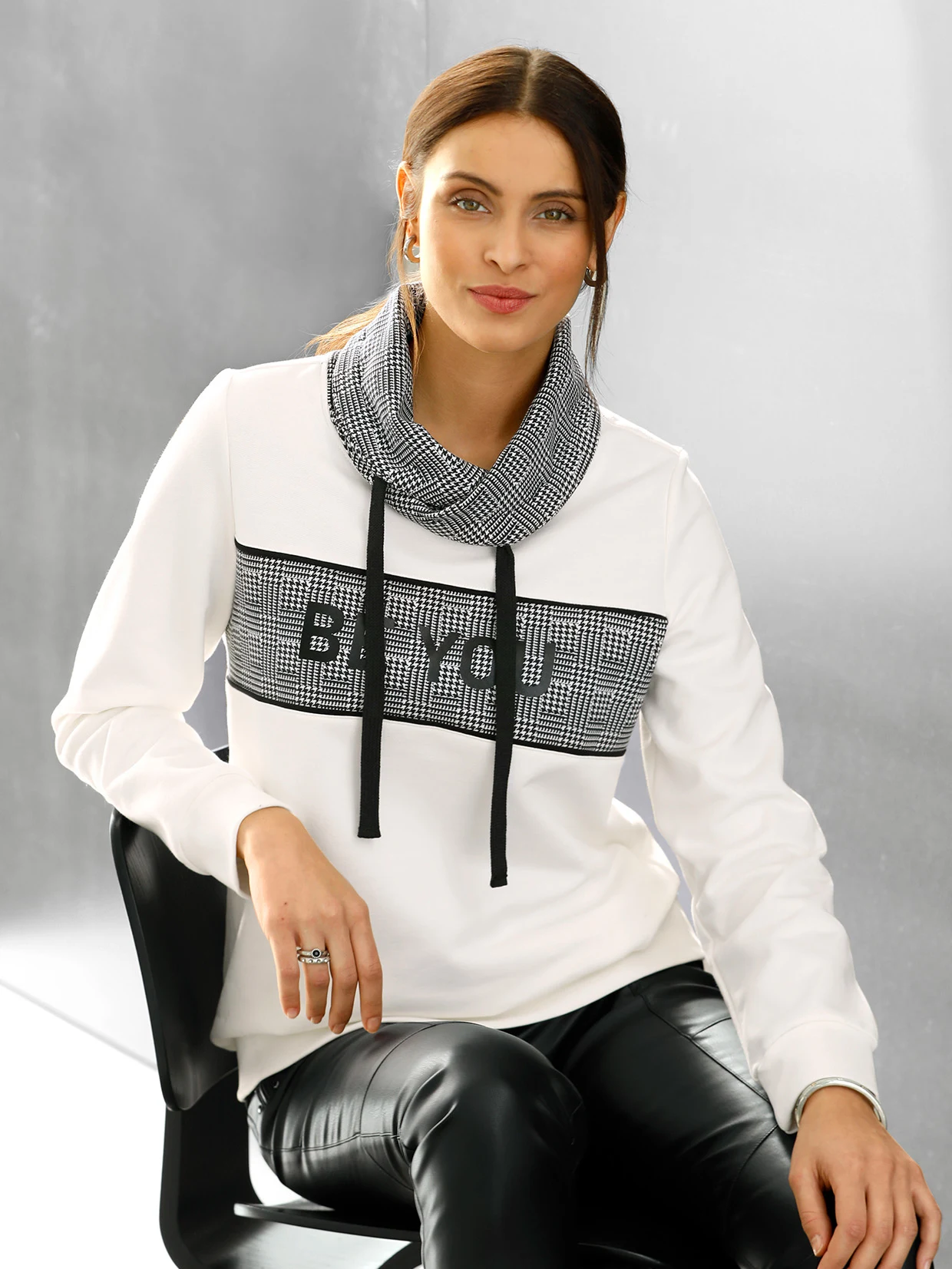 Weiße Sweatshirt mit schwarzem Karomuster und Schriftzug "Be You", kombiniert mit einer schwarzen Lederhose.