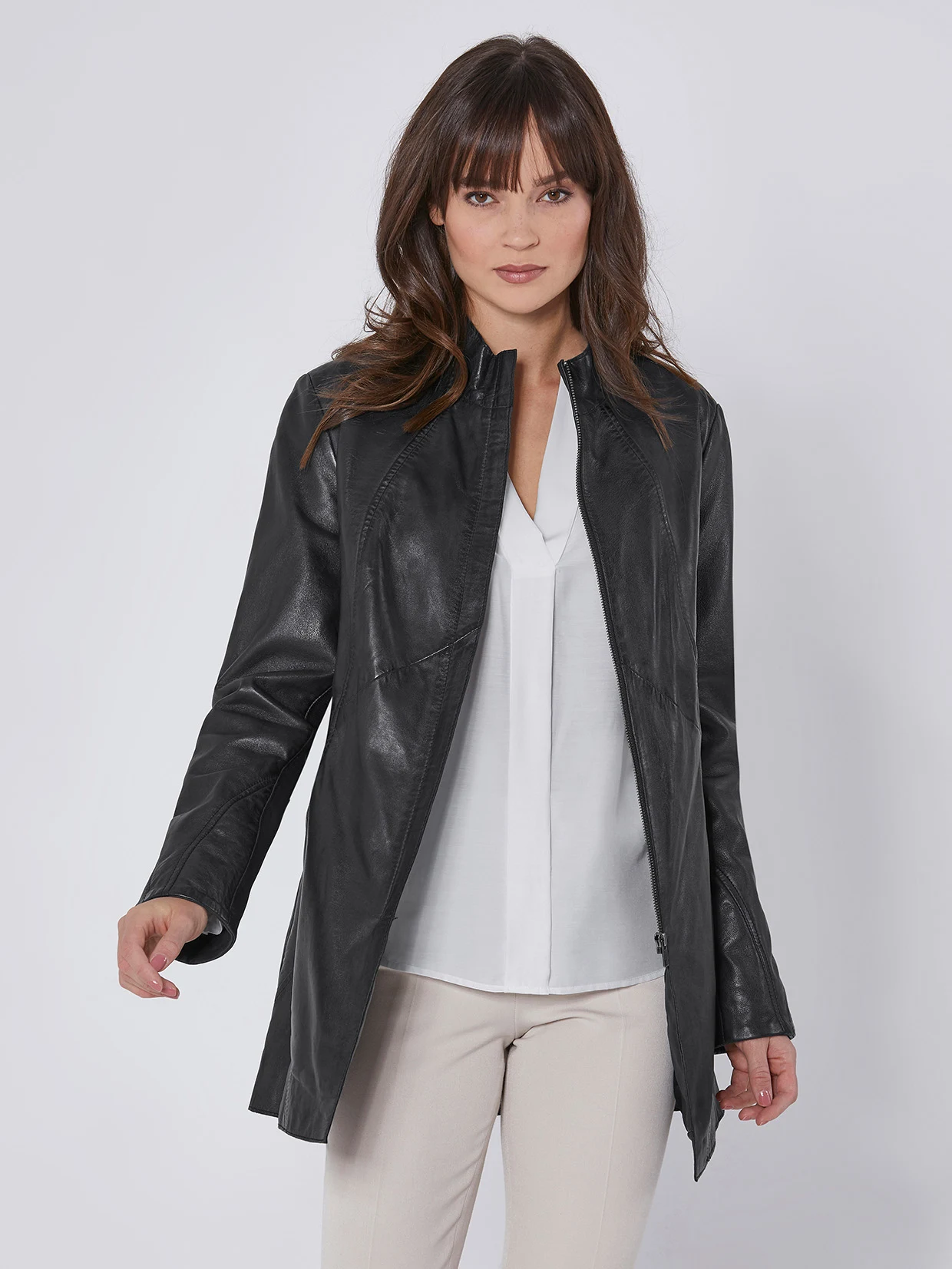 Zwarte leren jas voor dames, gecombineerd met een witte blouse en beige broek.