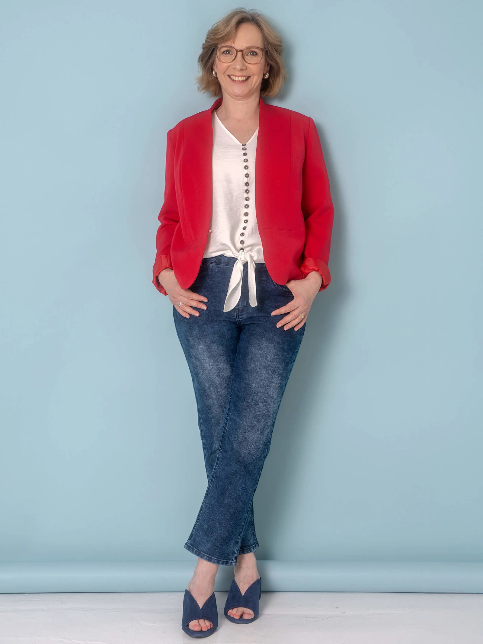 Eine Frau trägt einen roten Blazer über einem weißen Oberteil mit Knoten und blauen Jeans. Eine Frau trägt einen roten Blazer über einem weißen Oberteil mit Knoten und blauen Jeans.