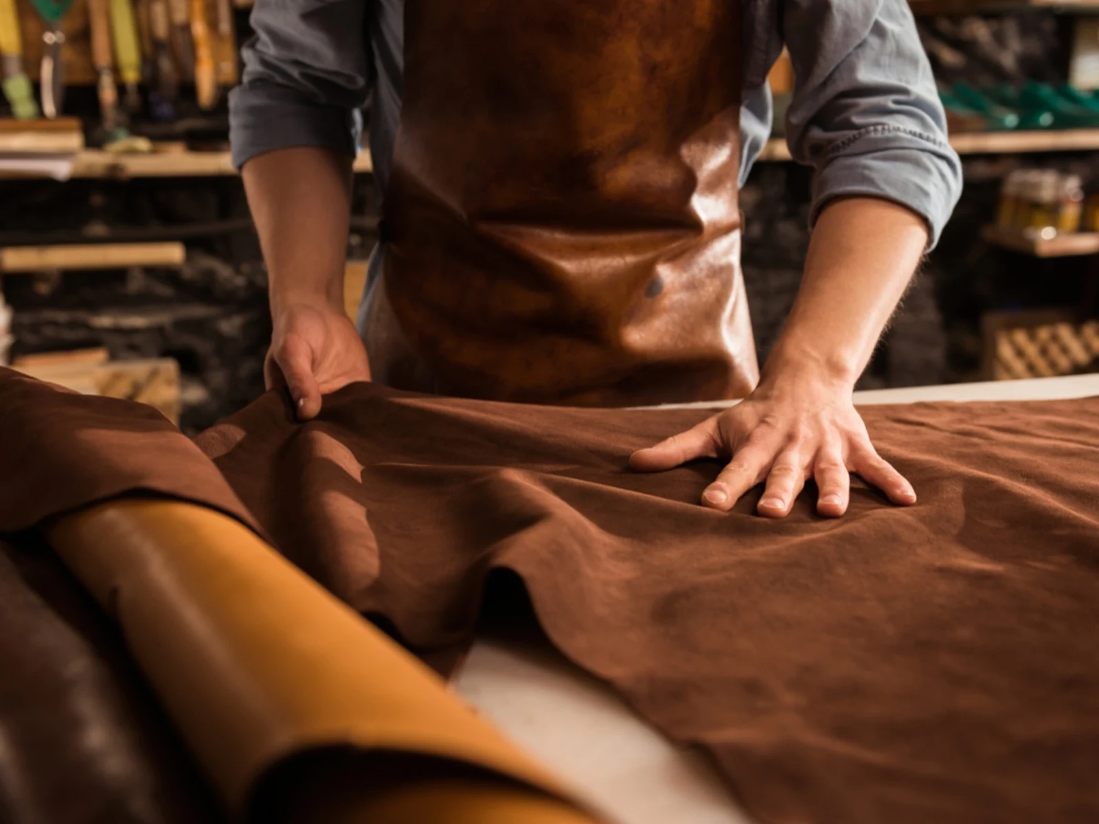 Handwerker in Lederschürze bearbeitet braunes Leder auf einer Werkbank. Handwerker in Lederschürze bearbeitet braunes Leder auf einer Werkbank.