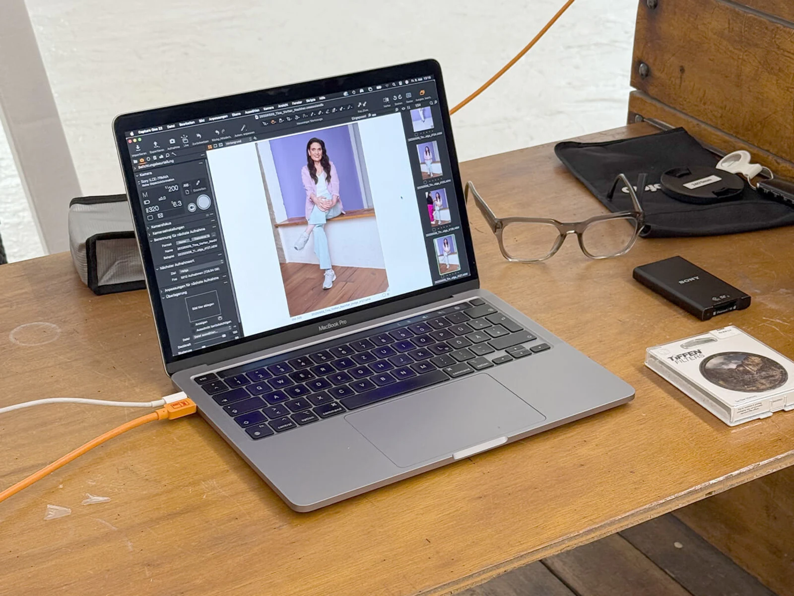 Ein Laptop zeigt ein Bild einer Frau auf dem Bildschirm, umgeben von Brille, Ladegerät und anderen Gegenständen auf einem Tisch. Ein Laptop zeigt ein Bild einer Frau auf dem Bildschirm, umgeben von Brille, Ladegerät und anderen Gegenständen auf einem Tisch.