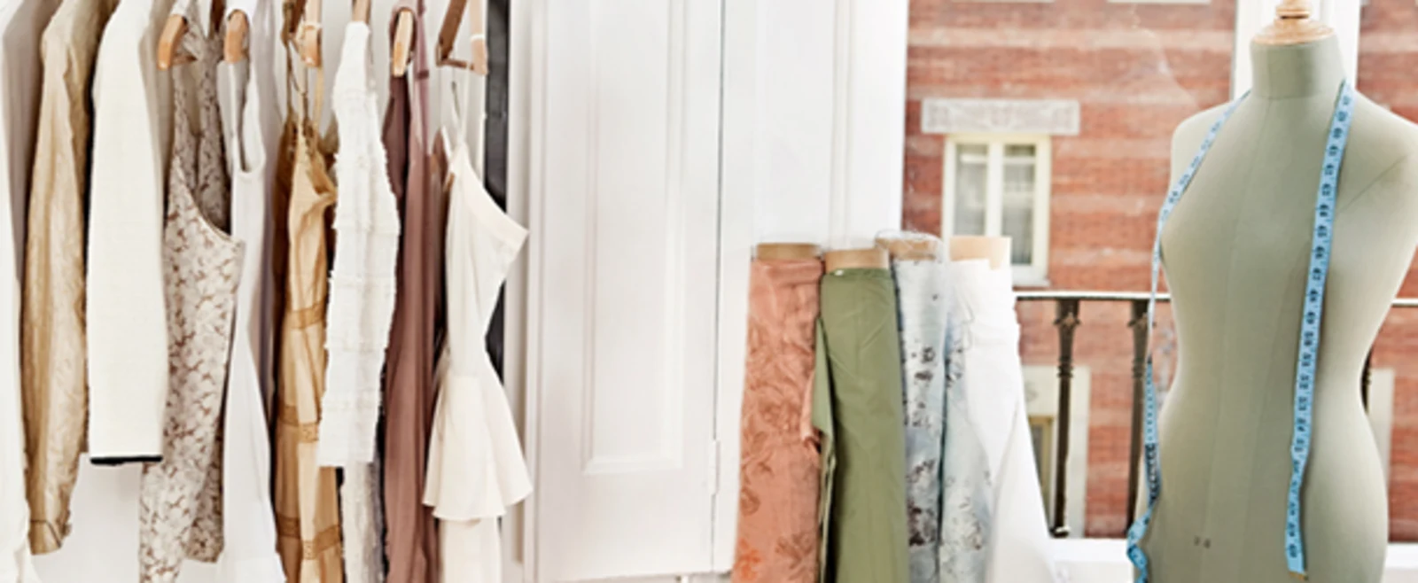 Kledingrekken met jurken, stofrollen en een paspop met meetlint in een lichte studio. Kledingrekken met jurken, stofrollen en een paspop met meetlint in een lichte studio.