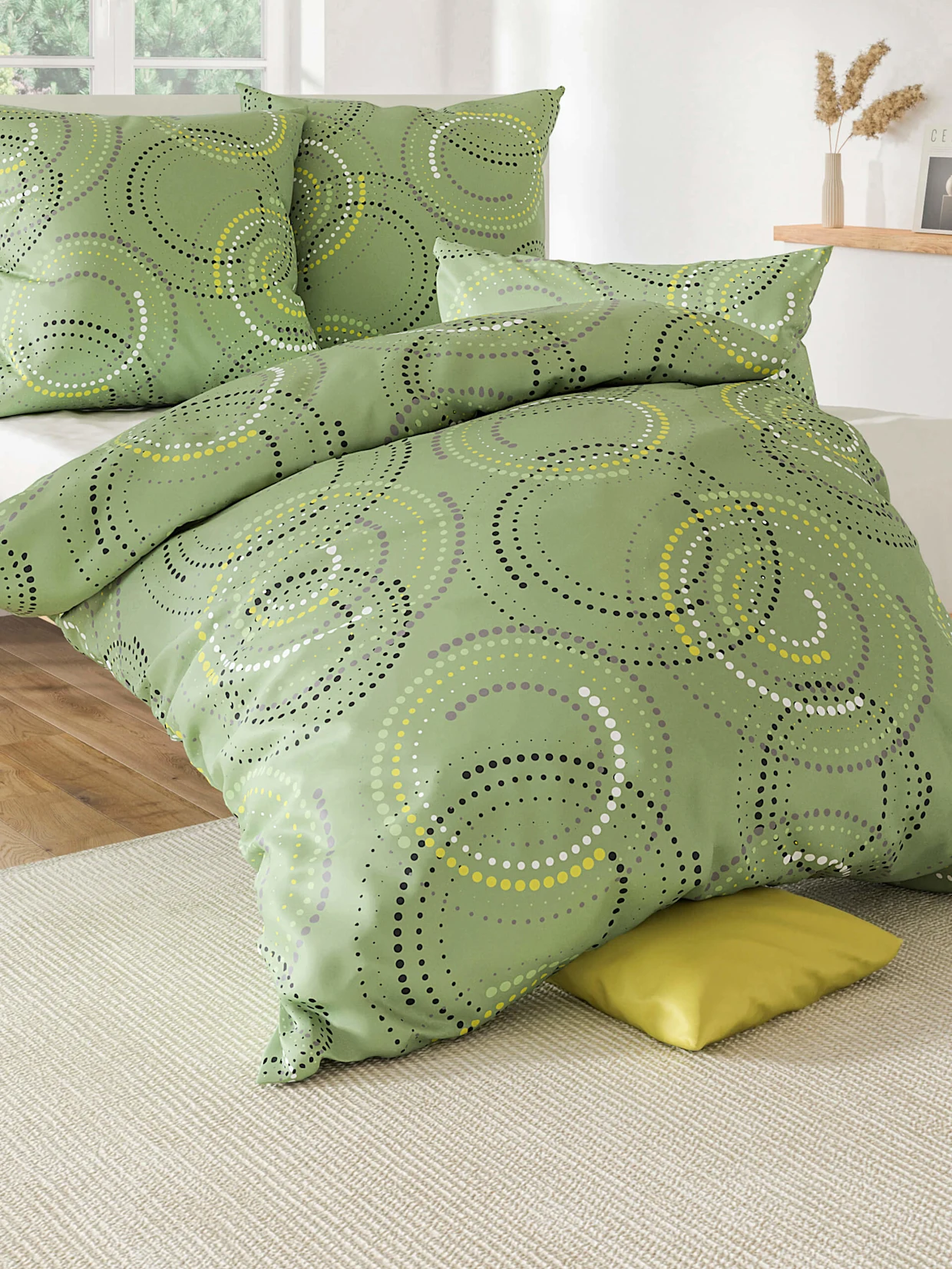 Ein Bett mit grün gemusterter Bettwäsche, bestehend aus Kissenbezügen und Decke, in einem hellen, modernen Schlafzimmer.