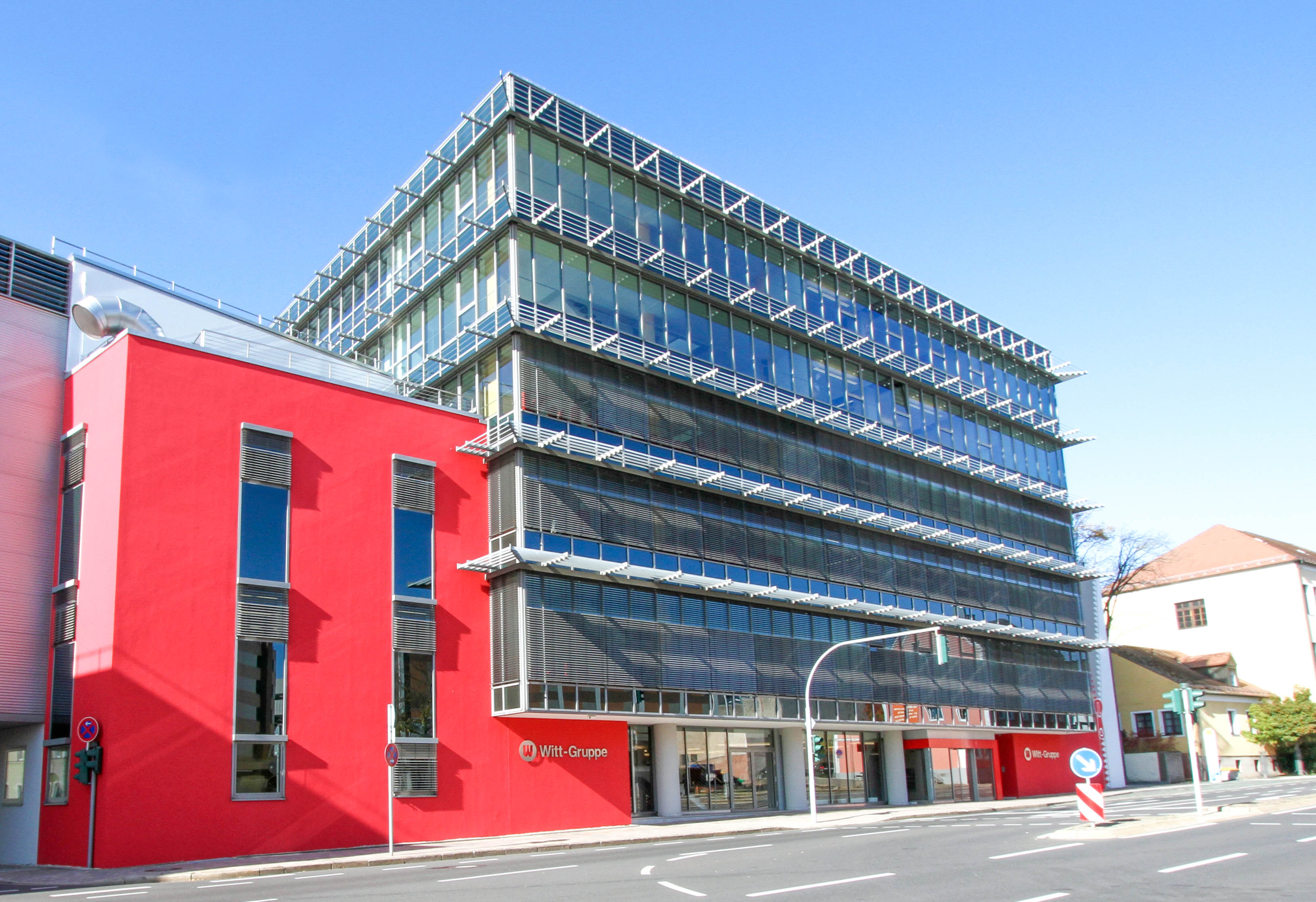 Modernes Bürogebäude mit roter und gläserner Fassade, Standort der Witt-Gruppe, bei sonnigem Himmel.