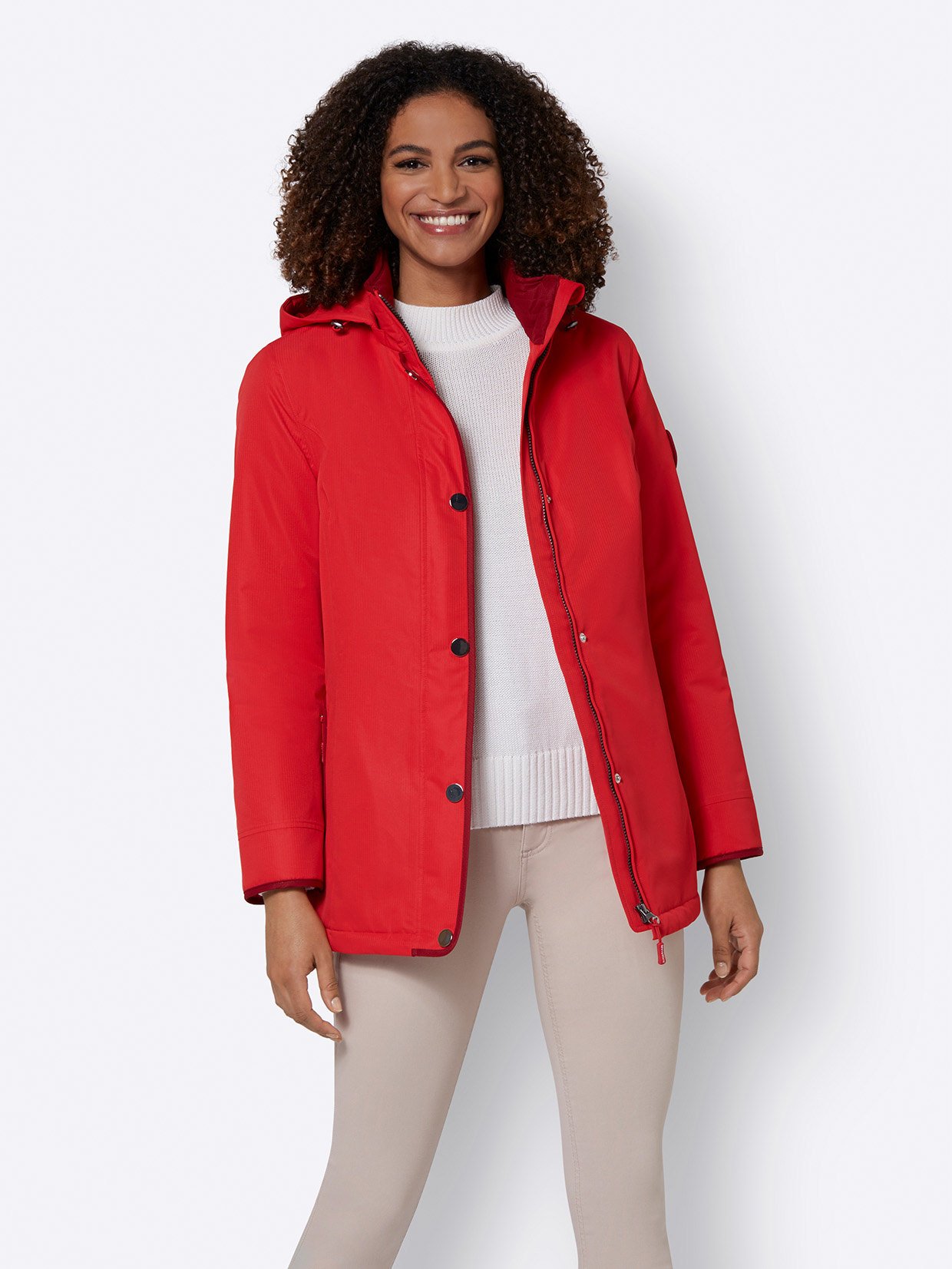 Rote Damenjacke mit Kapuze, Reißverschluss und Druckknöpfen, kombiniert mit weißem Pullover und hellbeiger Hose.
