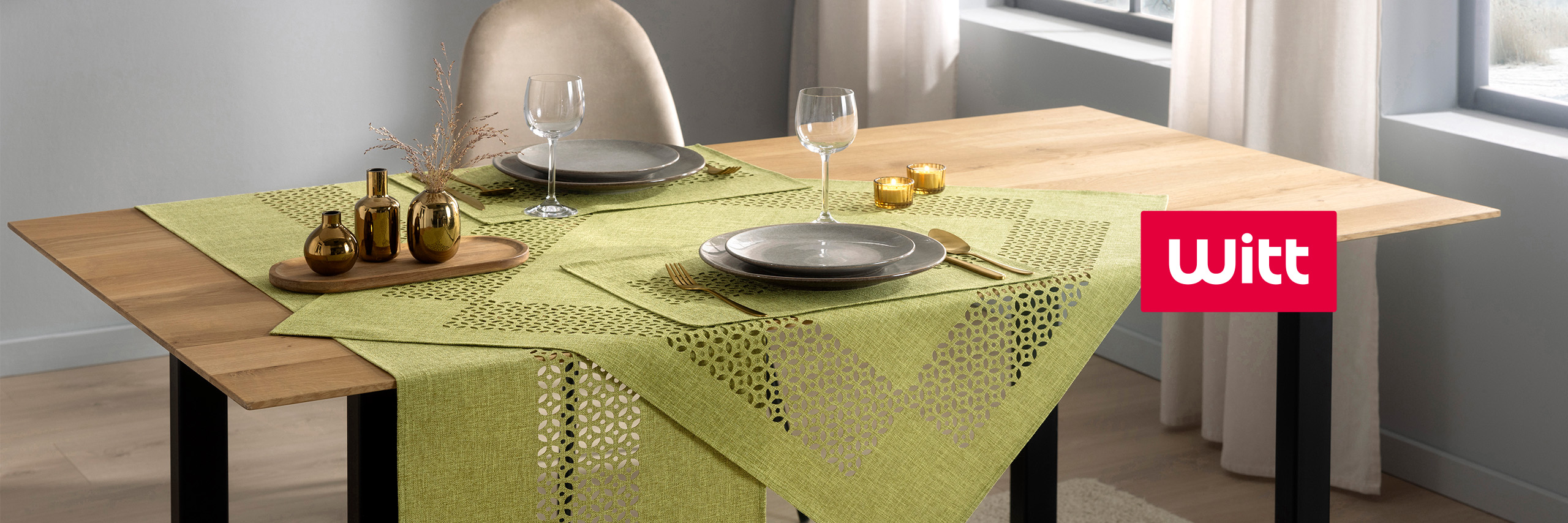 Holztisch mit hellgrüner Tischwäsche, Geschirr und goldenen Vasen festlich gedeckt. Witt-Logo rechts.