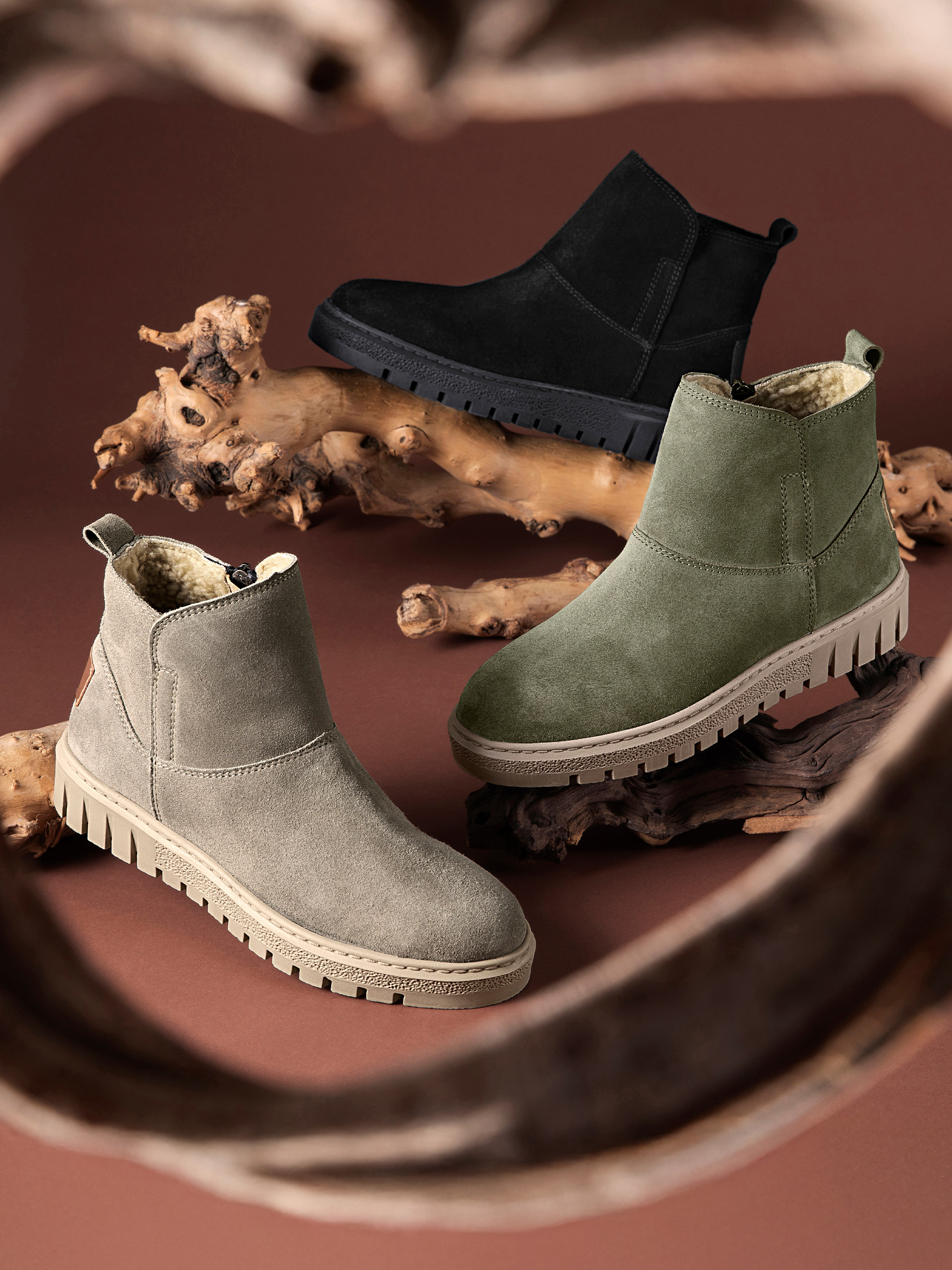 Drie paar gevoerde enkellaarsjes in zwart, olijfgroen en beige op een bruine achtergrond met decoratieve houtstukken.