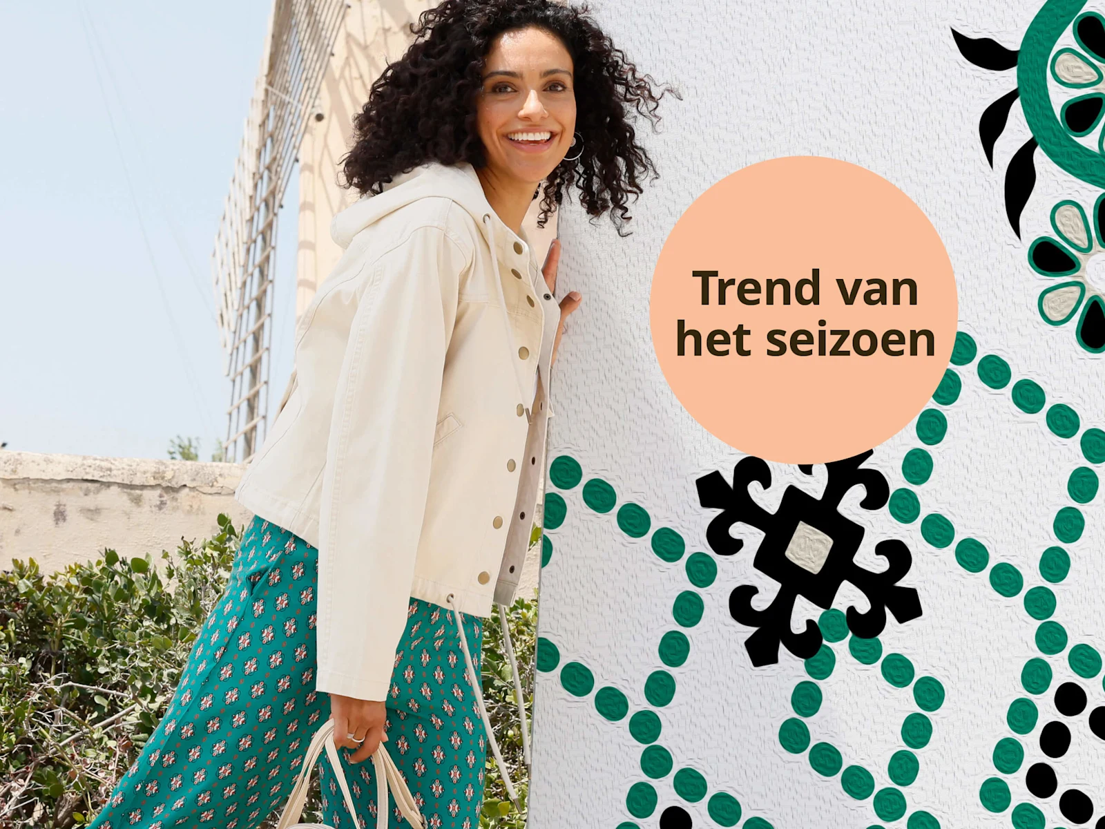 Een model draagt een crèmekleurig jasje en een groene broek met patroon, met daarnaast een oranje cirkel met de tekst 'Trend van het seizoen'.