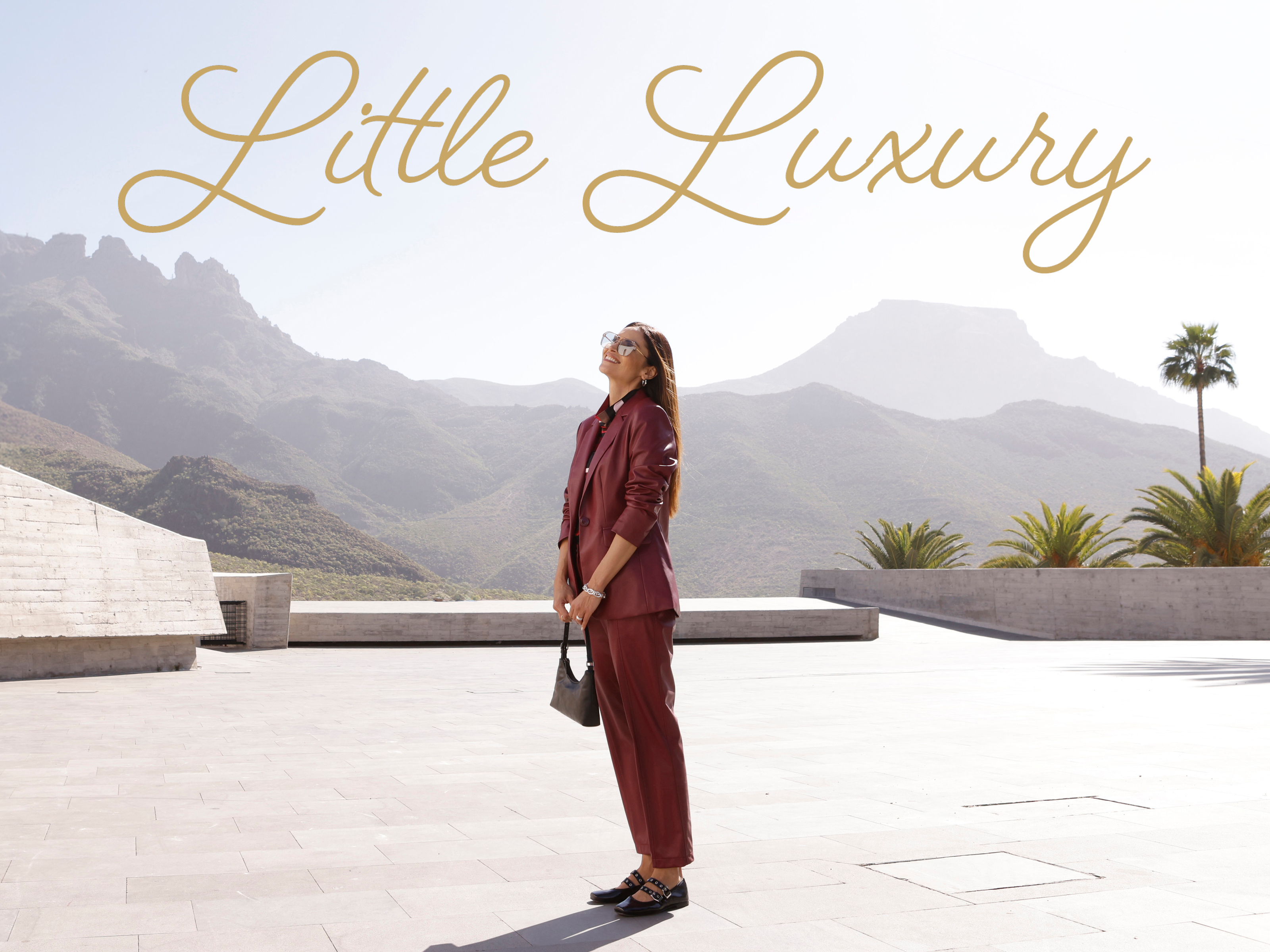 Model in een bordeauxrode blazer van imitatieleer, een broek en met het gouden opschrift “Little Luxury”