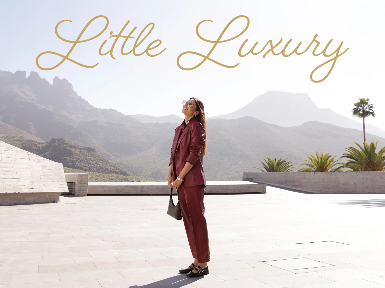 Model in een bordeauxrode blazer van imitatieleer, een broek en met het gouden opschrift “Little Luxury”