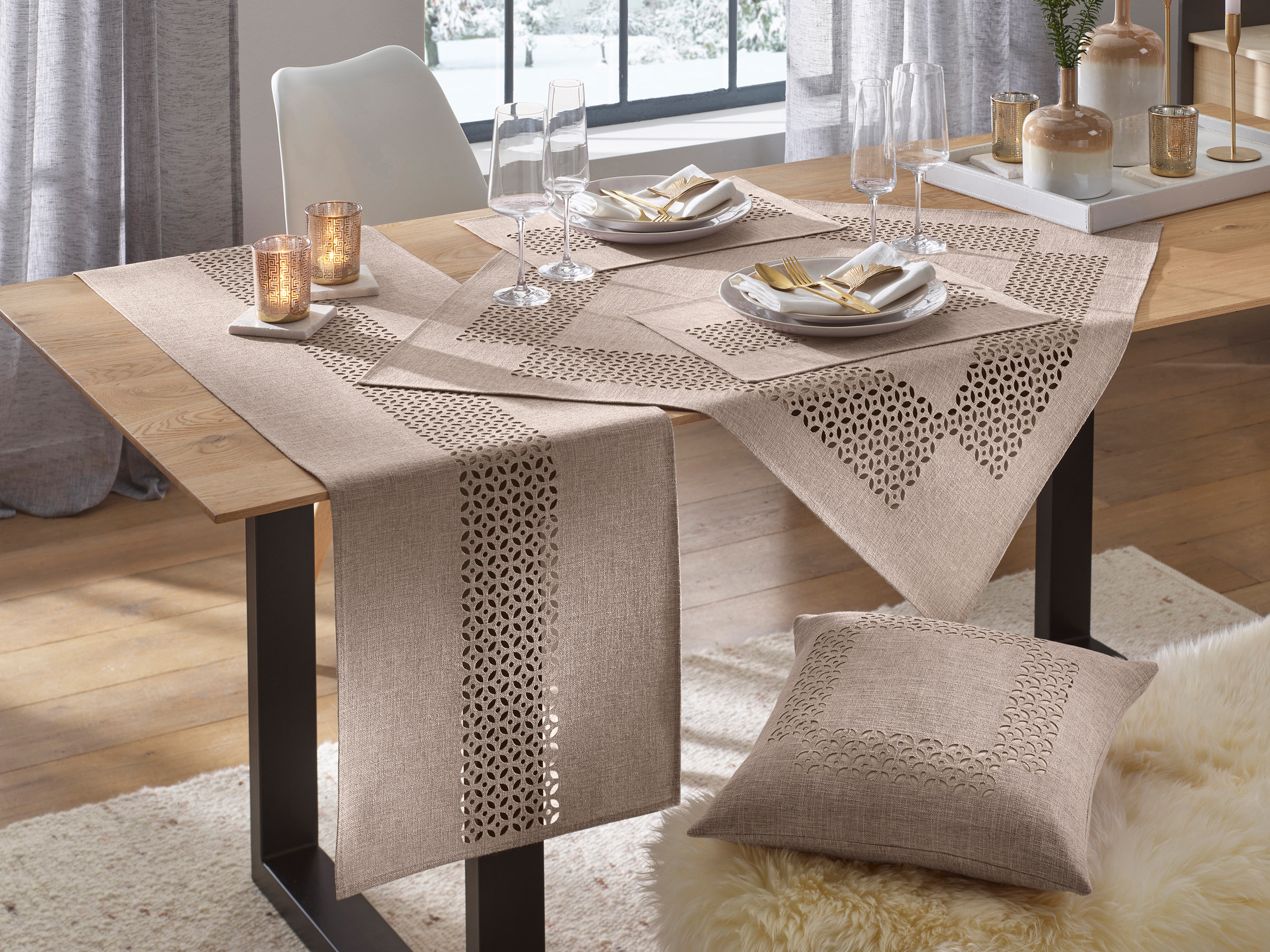 Esszimmertisch mit beigem, gemustertem Tischläufer und Tischdecke, gedeckt mit Tellern, Gläsern und Kerzen, dazu passendes Kissen auf Stuhl.