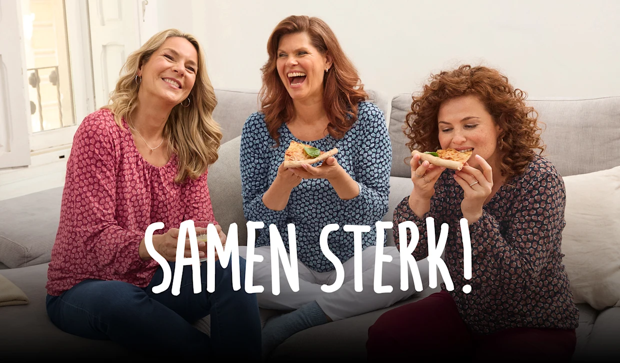 Een groep vrouwen zit lachend op een bank terwijl ze pizza eten. Op de foto staat “We houden elkaar bij elkaar” geschreven. Een groep vrouwen zit lachend op een bank terwijl ze pizza eten. Op de foto staat “We houden elkaar bij elkaar” geschreven.