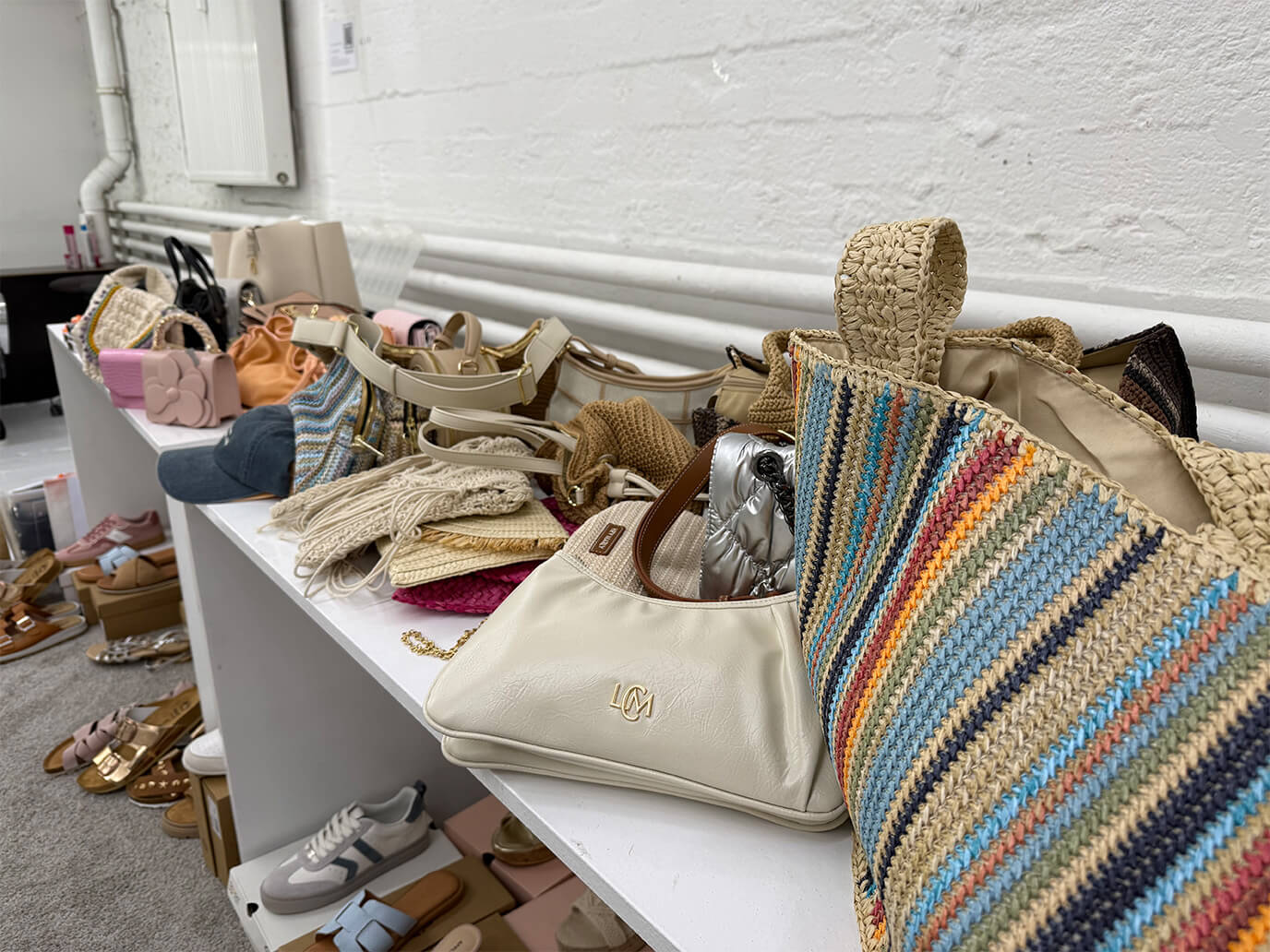 Handtaschen, Sandalen und Sneaker stehen dicht gedrängt auf einem weißen Regal.