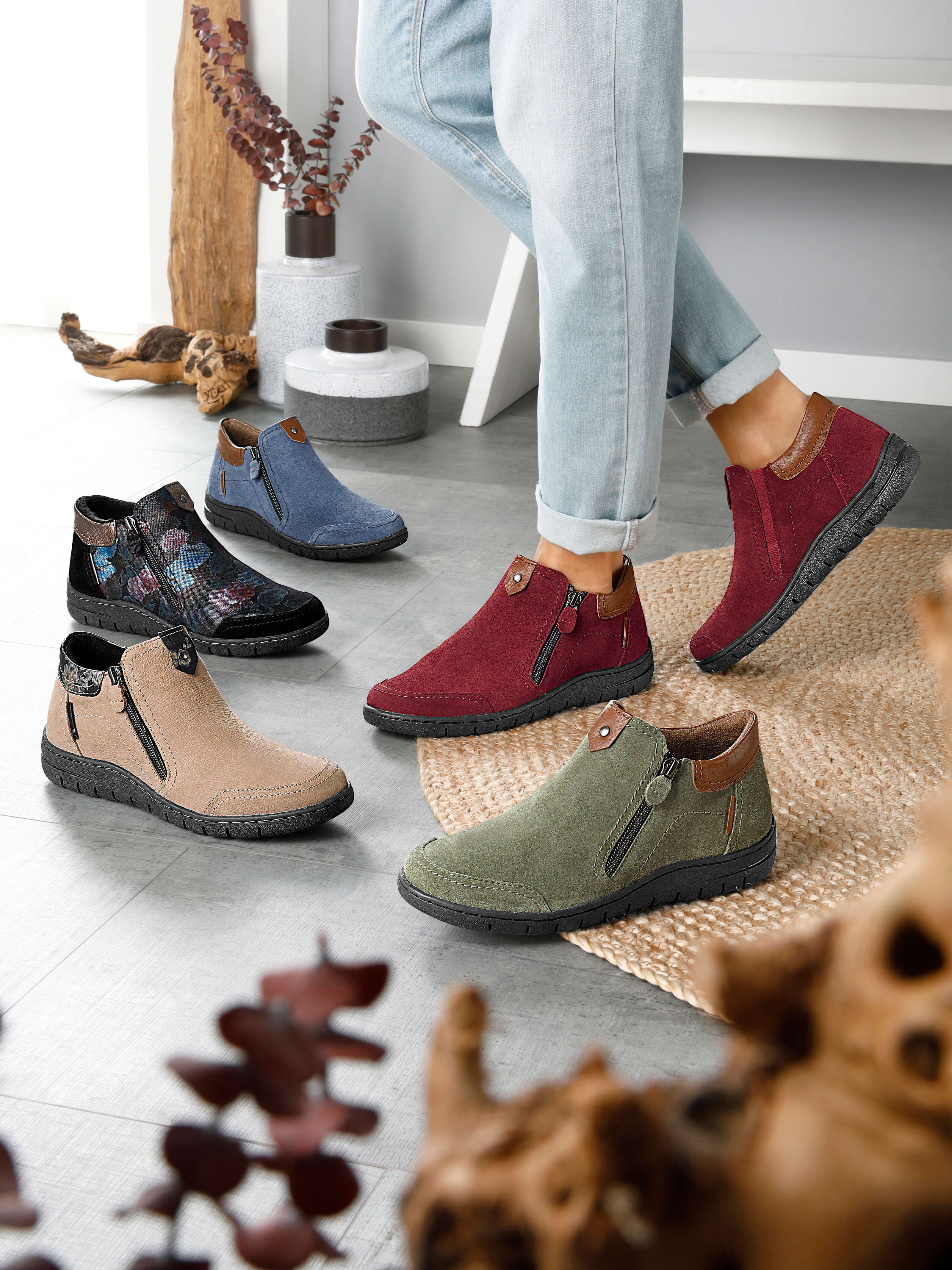Ein Model trägt rote Stiefeletten; weitere Stiefeletten in verschiedenen Farben stehen auf dem Boden.