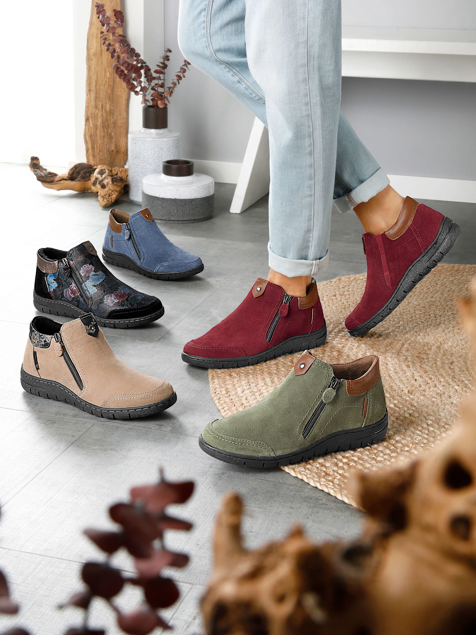 Ein Model trägt rote Stiefeletten; weitere Stiefeletten in verschiedenen Farben stehen auf dem Boden.