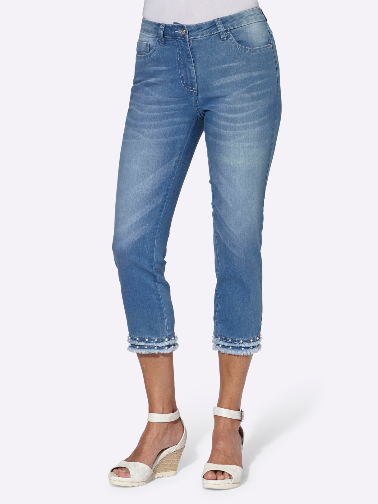 Damen-Jeans in Capri-Länge, hellblau mit Perlen- und Fransen-Dekor am Saum, kombiniert mit weißen Keilsandalen.