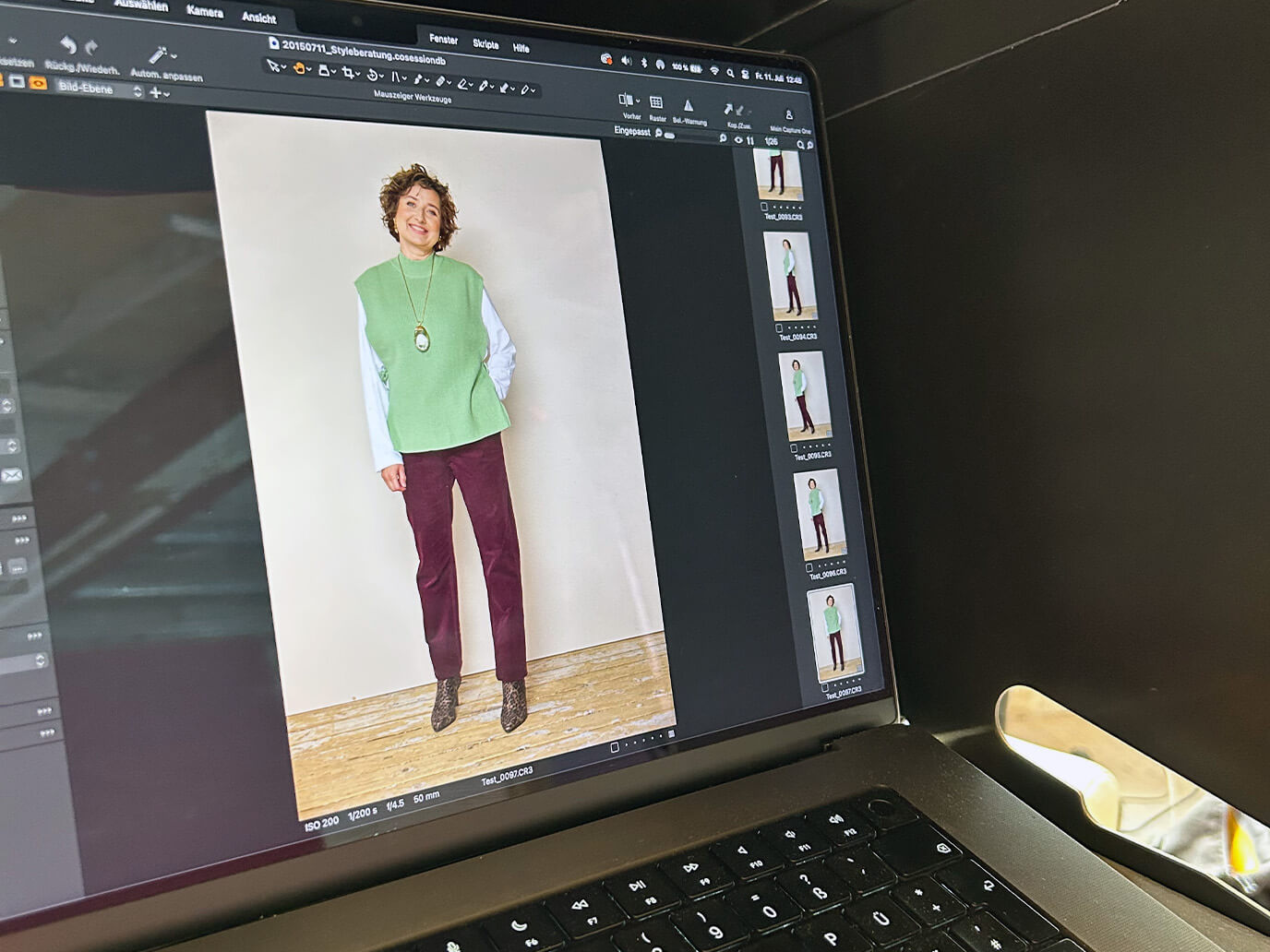 Bildschirm eines Laptops zeigt ein Foto einer Frau mit grünem ärmellosen Pullunder, weißem Langarmshirt, bordeauxroter Cordhose und Leo-Stiefeletten vor beigem Hintergrund.
