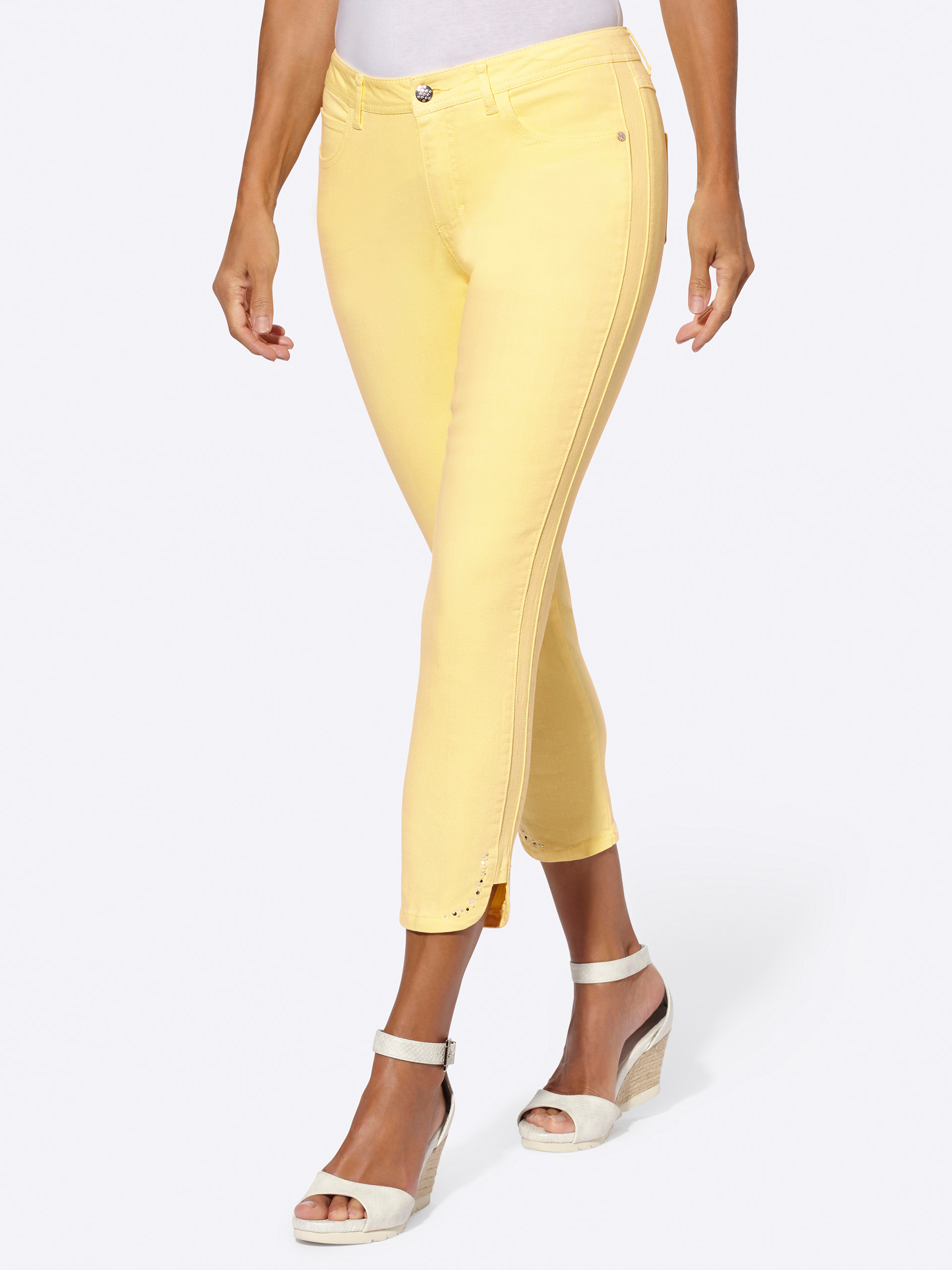 Gelbe Damenhose in Capri-Länge mit seitlichen Zierknöpfen, kombiniert mit beigen Keilsandaletten.