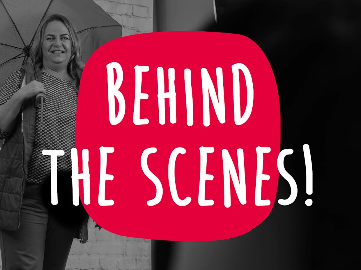 Eine Schwarz-Weiß Aufnahme, die eine Frau mit einem Regenschirm in einem Fotostudio zeigt, mit einem großen roten Kreis in der Mitte, auf dem in weißen Großbuchstaben 'BEHIND THE SCENES!' steht. Eine Schwarz-Weiß Aufnahme, die eine Frau mit einem Regenschirm in einem Fotostudio zeigt, mit einem großen roten Kreis in der Mitte, auf dem in weißen Großbuchstaben 'BEHIND THE SCENES!' steht.