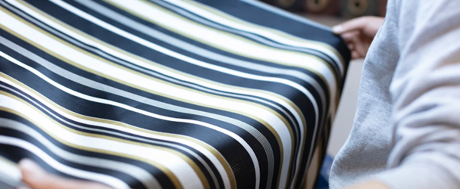 Gestreepte stof in zwart, wit en geel wordt vastgehouden door een persoon. Gestreepte stof in zwart, wit en geel wordt vastgehouden door een persoon.