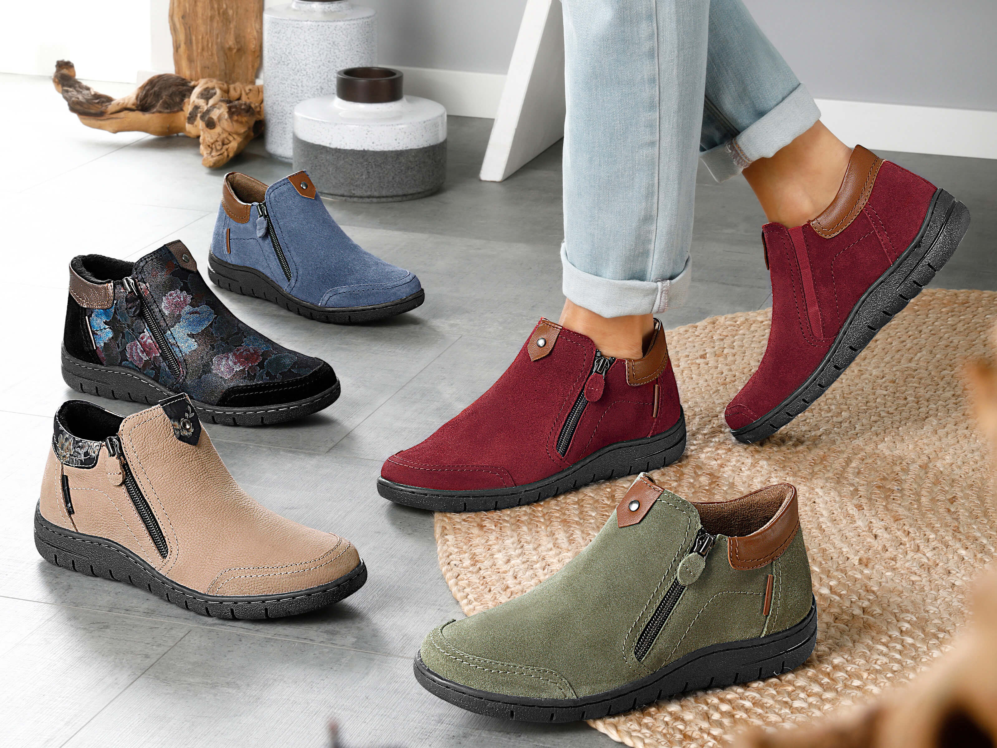 Ein Model trägt rote Stiefeletten; weitere Stiefeletten in verschiedenen Farben stehen auf dem Boden.
