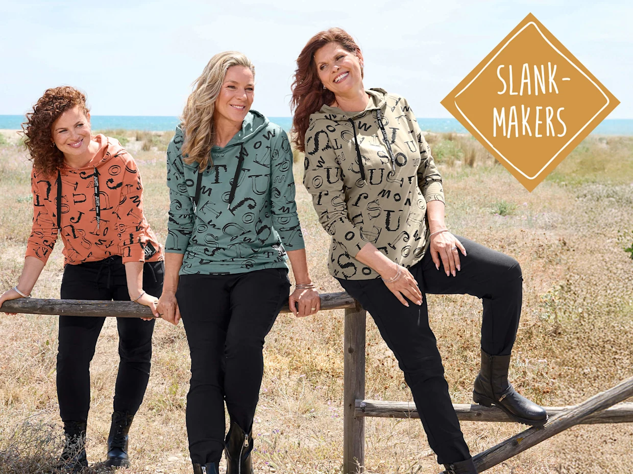 Drie modellen in bedrukte hoodies en donkere broeken poseren buiten. Tekst op een gouden ruit: 'Slankmakers'.