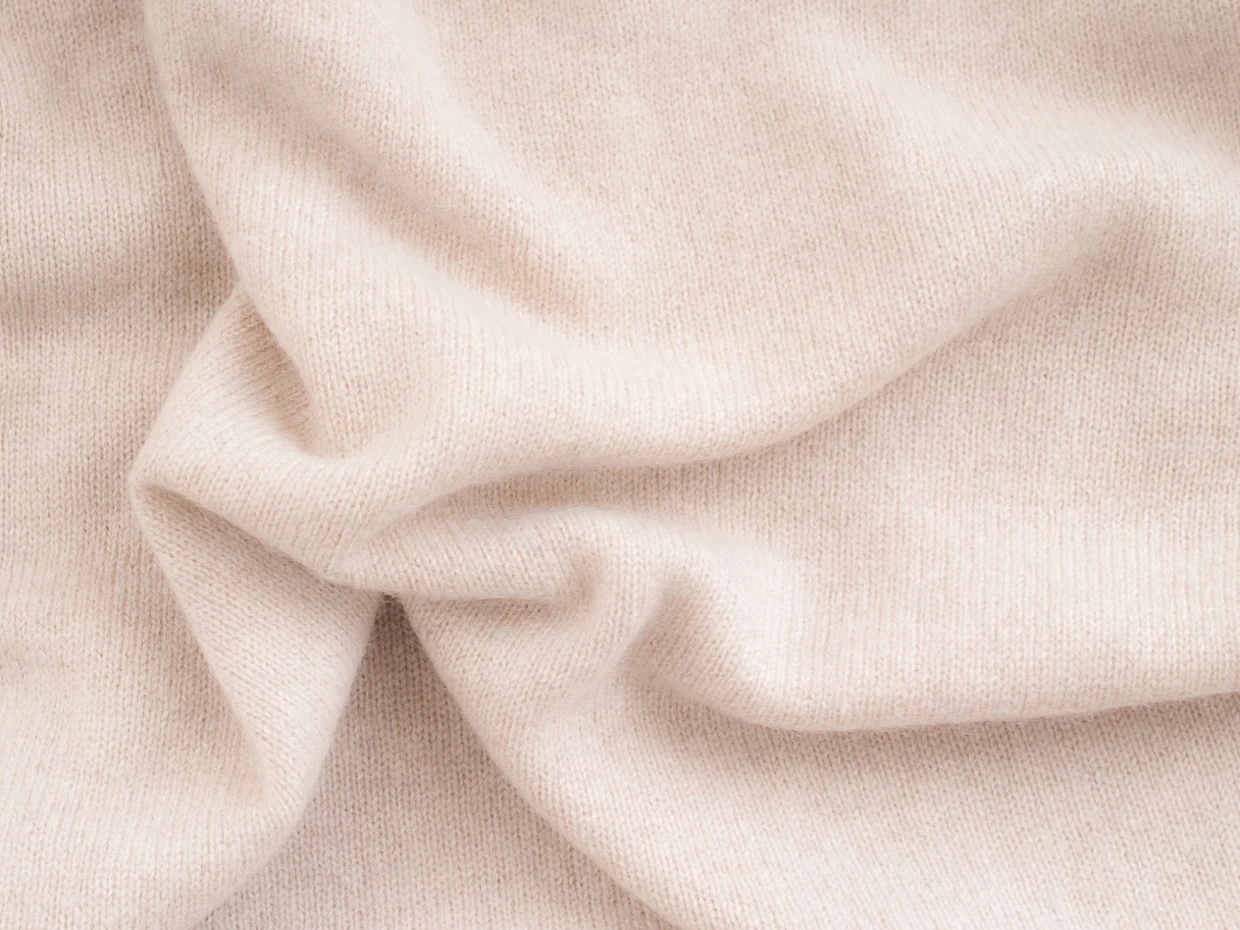 Weicher, beigefarbener Strickstoff mit feiner Textur und Falten. Weicher, beigefarbener Strickstoff mit feiner Textur und Falten.