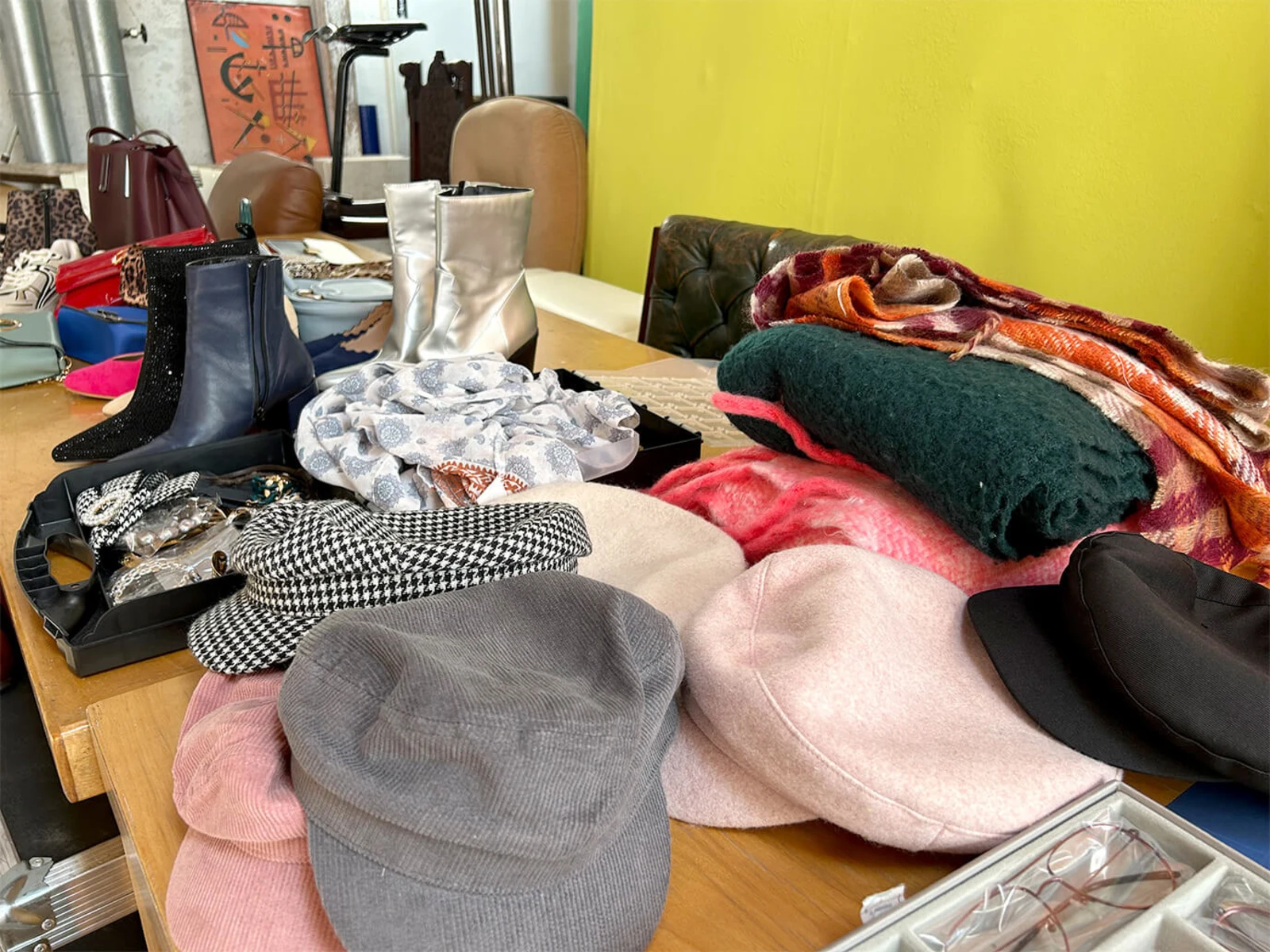 Verschiedene Hüte, Schals, Stiefel und Accessoires liegen auf einem Holztisch vor einer grünen Wand. Verschiedene Hüte, Schals, Stiefel und Accessoires liegen auf einem Holztisch vor einer grünen Wand.