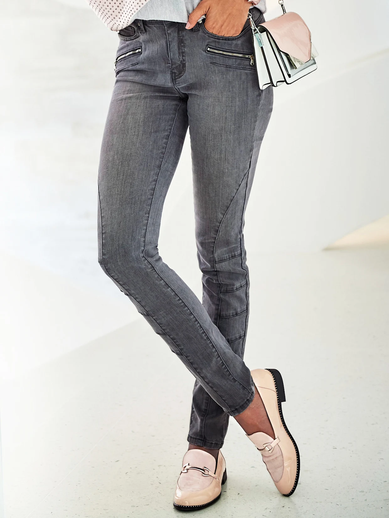 Graue Damenjeans mit Zierreißverschlüssen, kombiniert mit hellrosafarbenen Loafern und einer passenden Handtasche. Graue Damenjeans mit Zierreißverschlüssen, kombiniert mit hellrosafarbenen Loafern und einer passenden Handtasche.