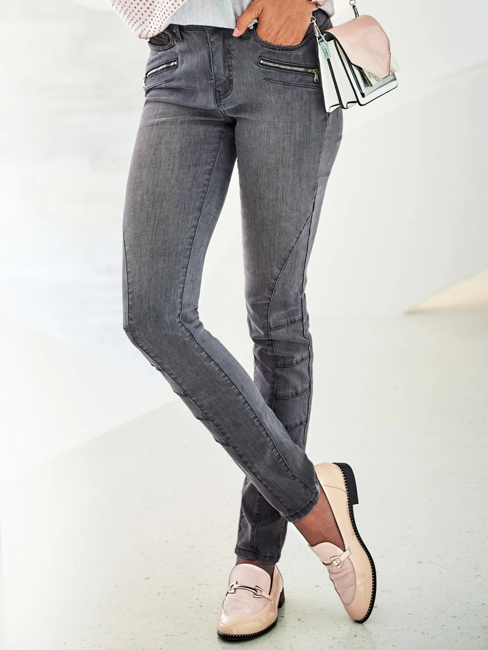 Graue Damenjeans mit Zierreißverschlüssen, kombiniert mit hellrosafarbenen Loafern und einer passenden Handtasche. Graue Damenjeans mit Zierreißverschlüssen, kombiniert mit hellrosafarbenen Loafern und einer passenden Handtasche.