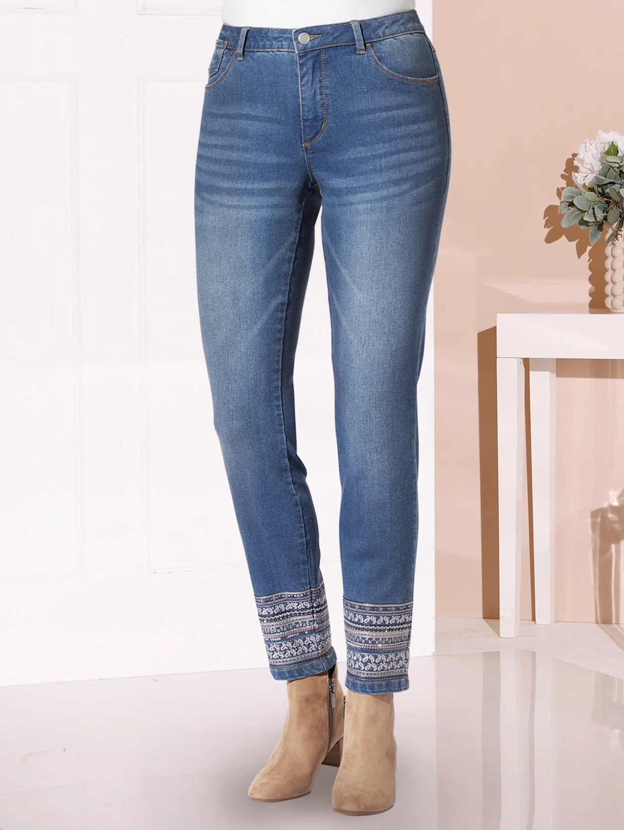 Damenjeans in Blau mit Stickmuster am Saum, kombiniert mit beigefarbenen Stiefeletten.