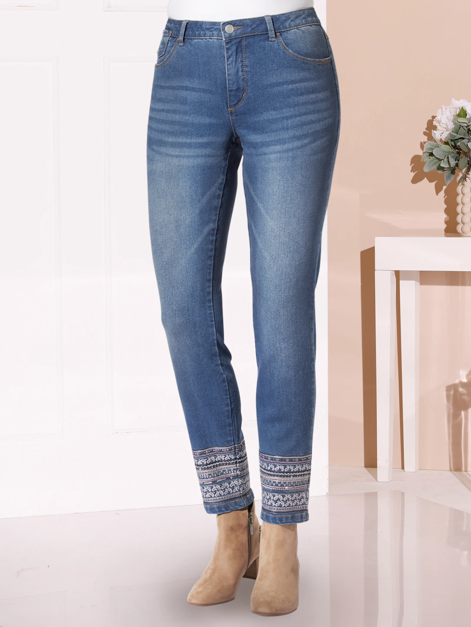 Damenjeans in Blau mit Stickmuster am Saum, kombiniert mit beigefarbenen Stiefeletten.