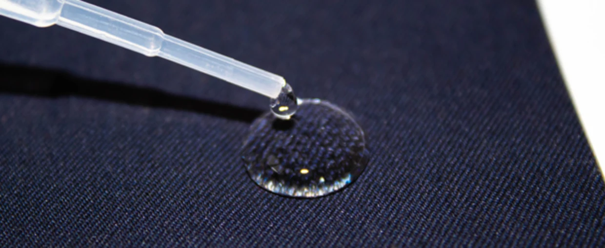 Wassertropfen aus einer Pipette auf wasserabweisendem dunkelblauem Stoff. Wassertropfen aus einer Pipette auf wasserabweisendem dunkelblauem Stoff.