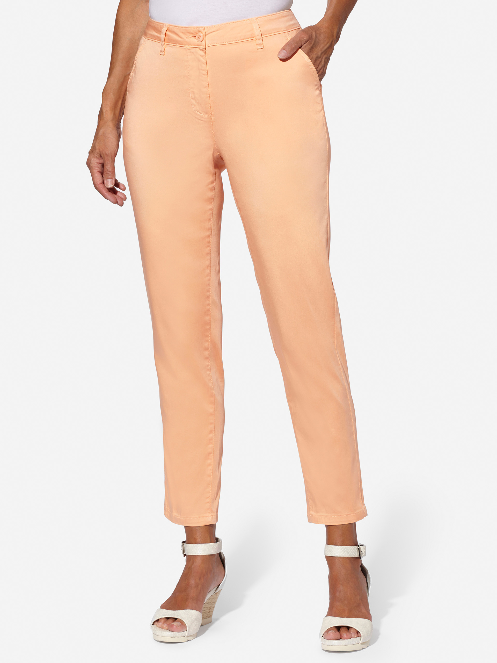 Damenhose in Pfirsichfarbe, knöchellang, mit Taschen und Knopfverschluss, kombiniert mit weißen Sandaletten mit Absatz.