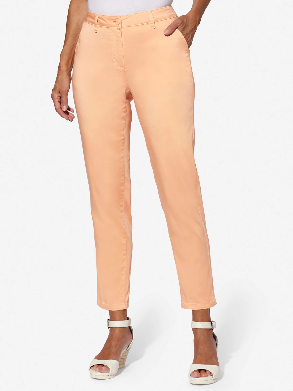 Vrouw draagt een perzikkleurige broek met hoge taille, gecombineerd met witte sandalen met sleehak.