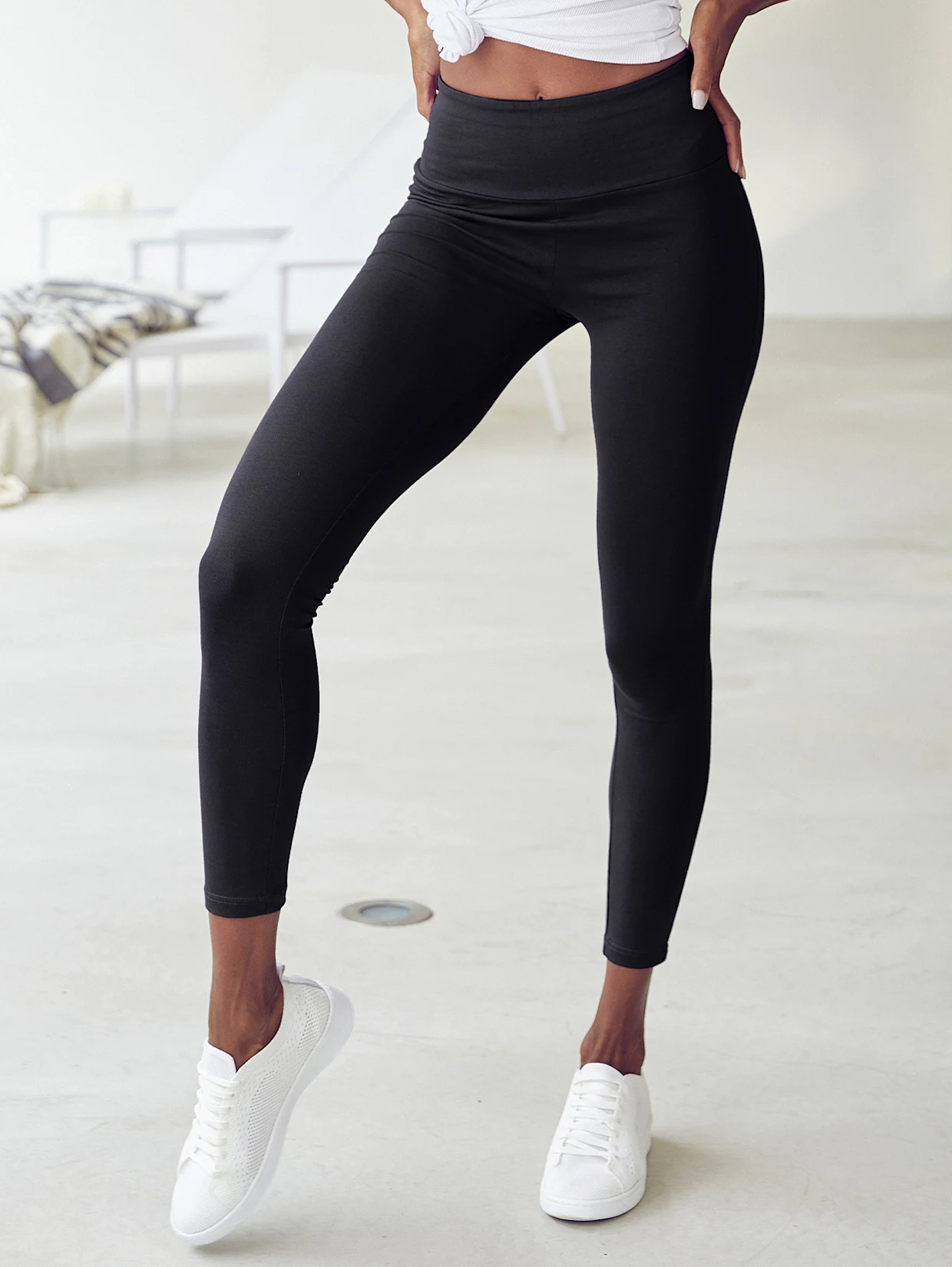 Schwarze Damen-Leggings mit hohem Bund, kombiniert mit weißen Sneakern, vor hellem Hintergrund. Schwarze Damen-Leggings mit hohem Bund, kombiniert mit weißen Sneakern, vor hellem Hintergrund.