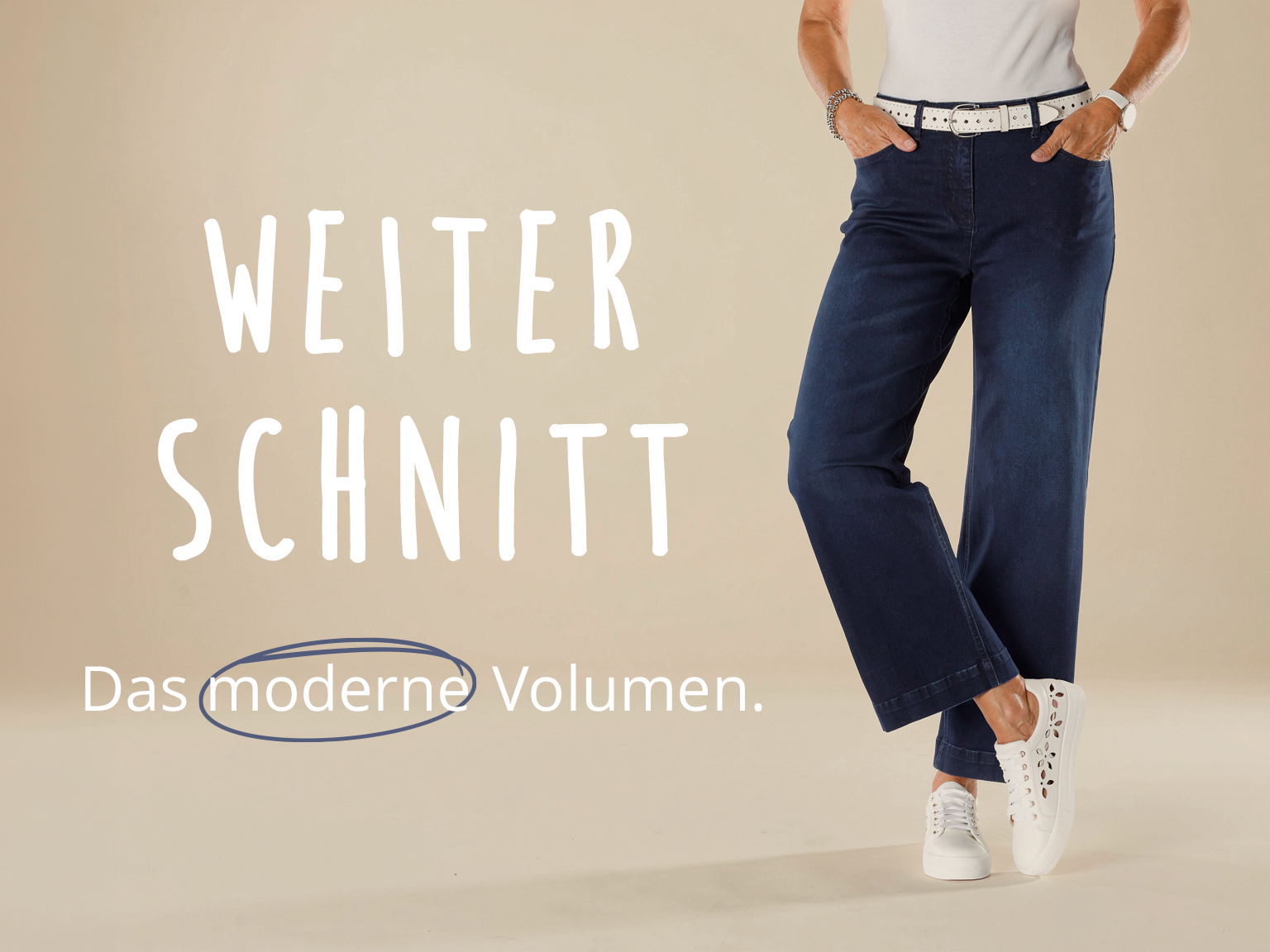 Frau in weiter Jeans mit weißem Gürtel und Sneakern. Text: Weiter Schnitt – Das moderne Volumen.