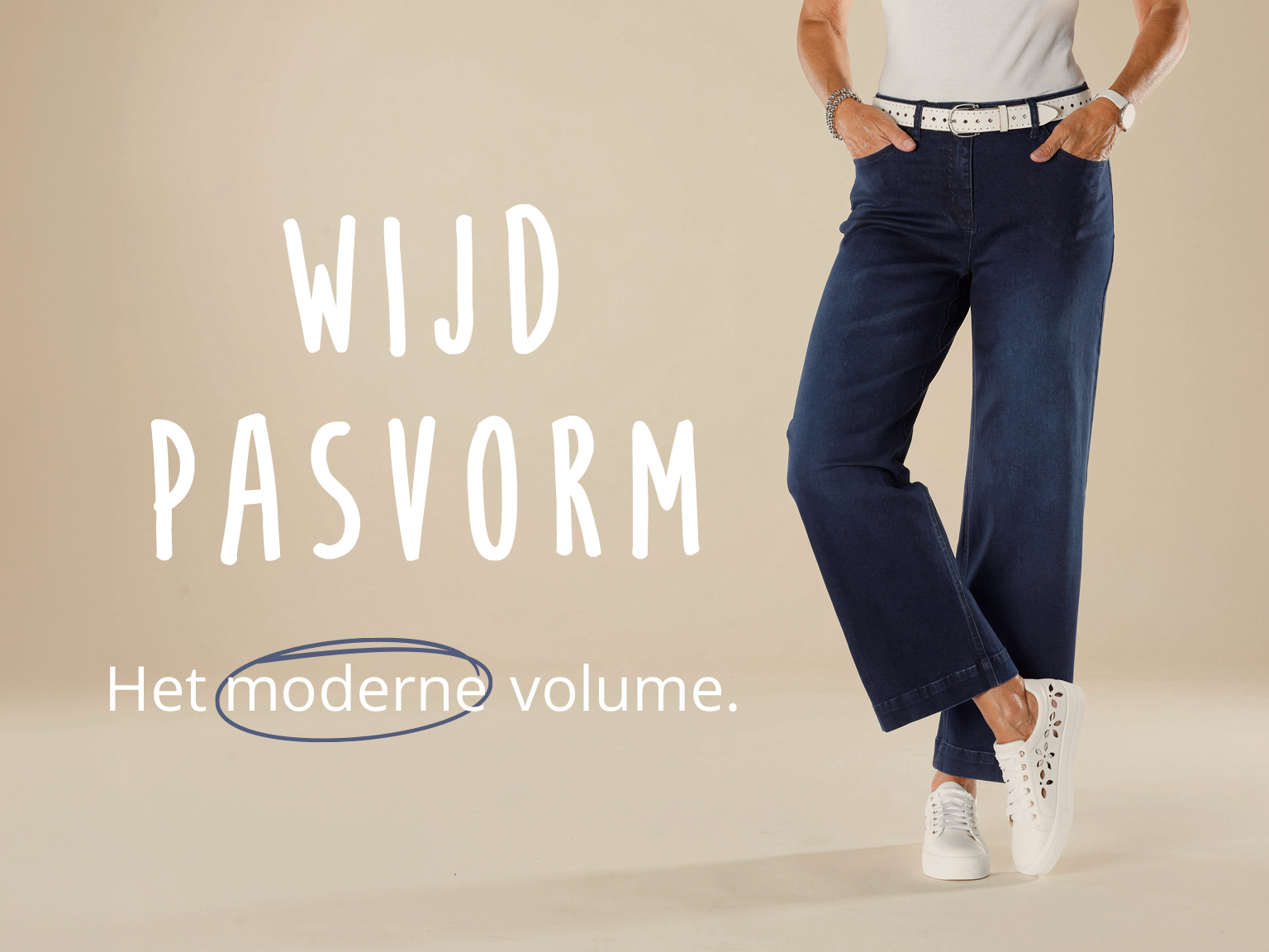 Vrouw in wijde jeans met witte riem en sneakers. Tekst: Wijd pasvorm – Het moderne volume.