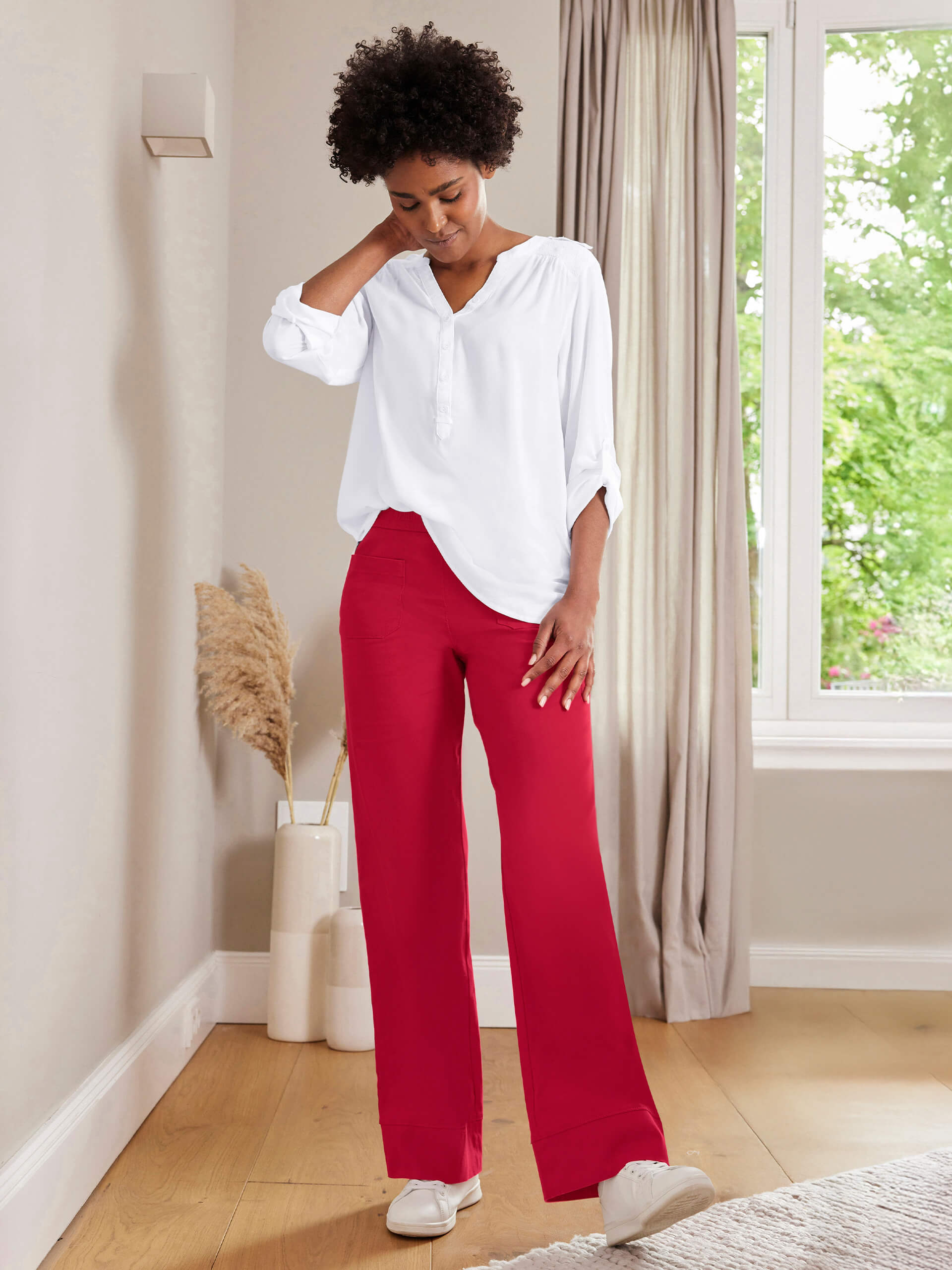 Ein Model steht in einem hellen Raum, trägt ein weißes Oberteil und rote, weite Hosen, mit weißen Sneakers.