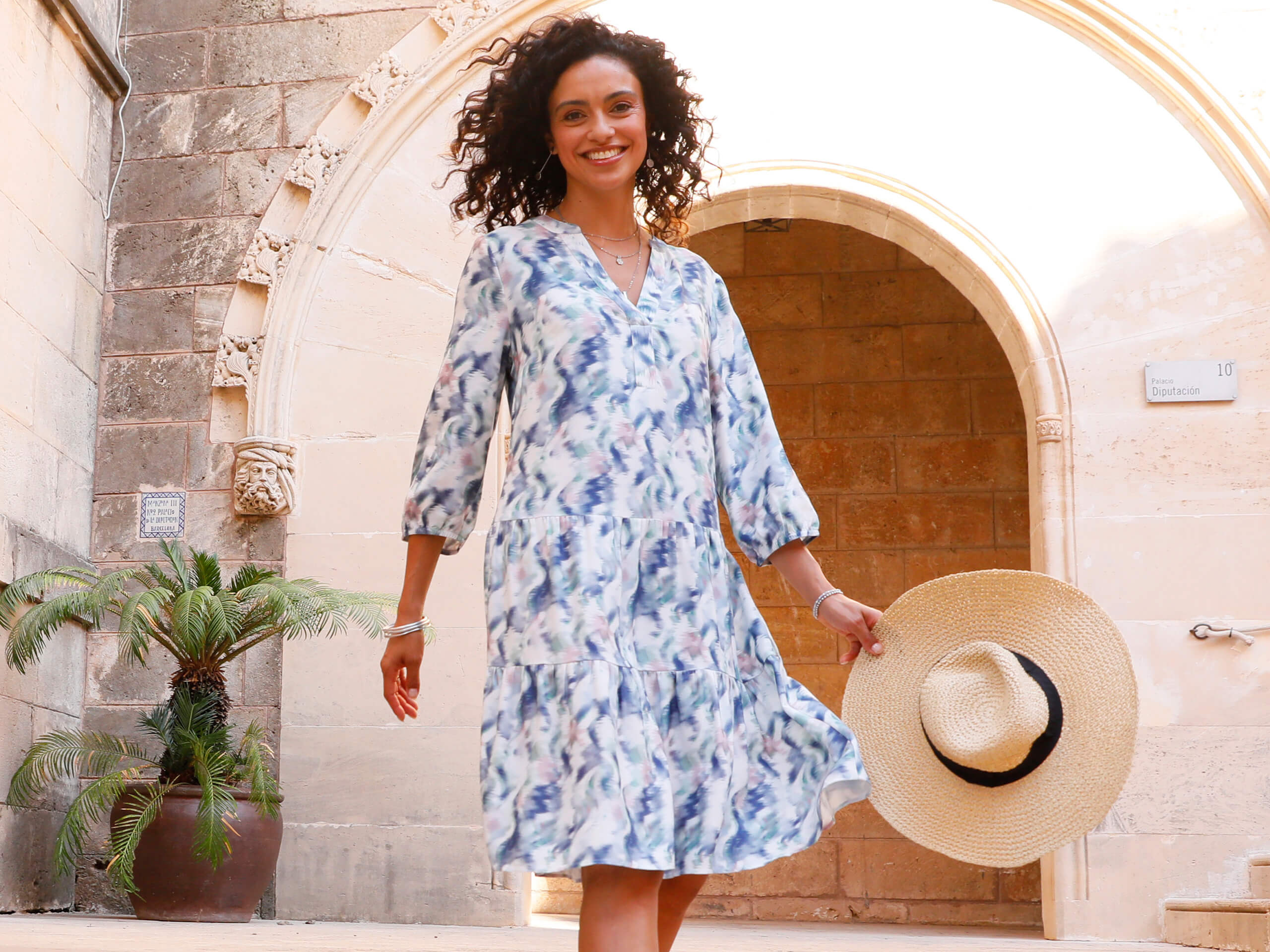 Frau in ecru-jeansblau-bedrucktem Kleid in Stufenform mit kombiniertem Rundhals-V-Ausschnitt, Raffung am Ausschnitt hinten und 3/4-Ärmeln mit elastischem Gummizug